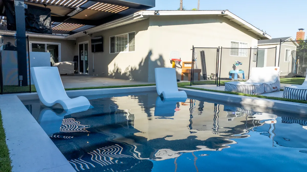 In-water loungers on the tanning shelf, the pergola and house standing behind the deep blue water.