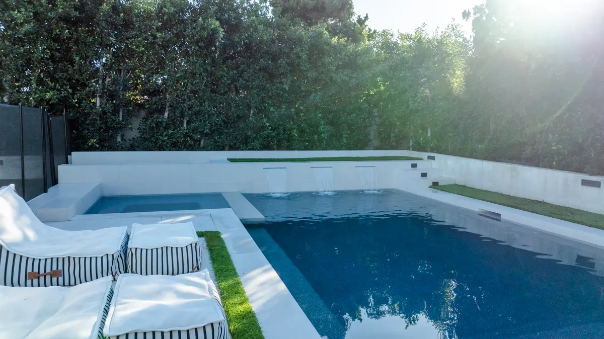 Striped daybeds on the deck beside the pool, turf running between the paving and the water.