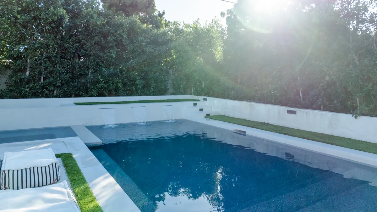 The pool in low afternoon sun, its rendered walls pale against the deep blue water.