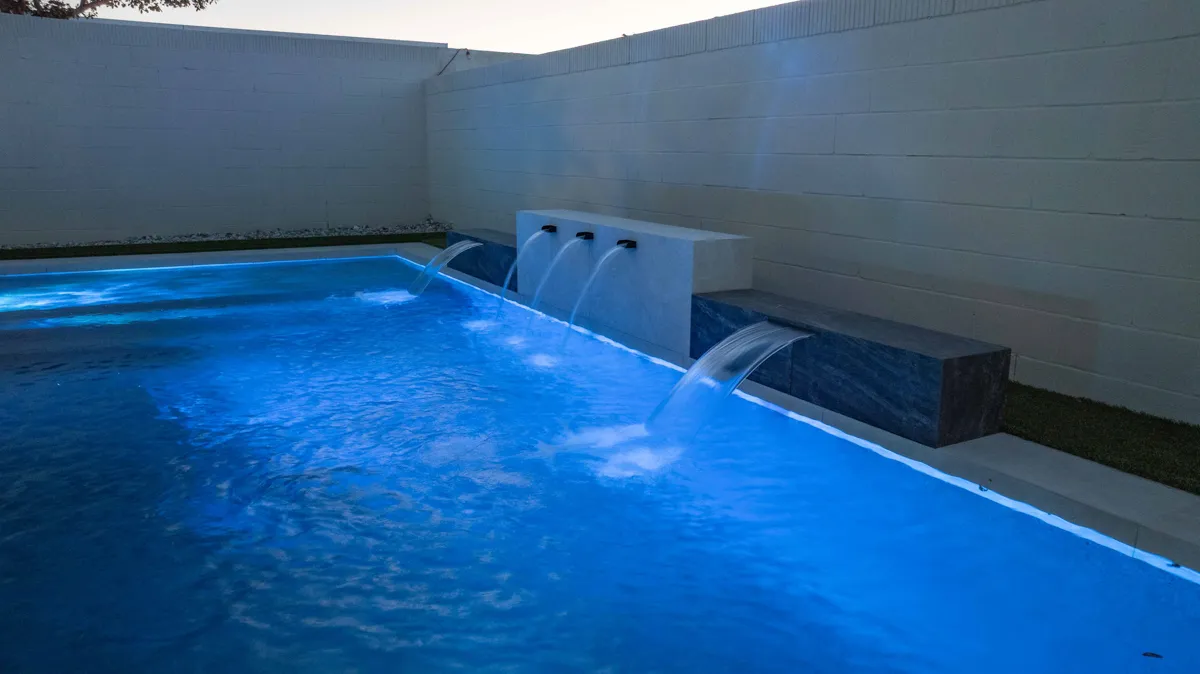 The pool lit deep blue after dark, sheet waterfalls falling from a raised wall into the deep end.