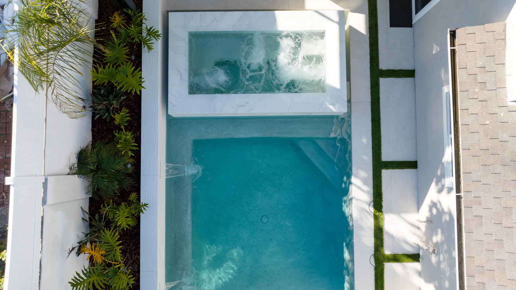 The pool and raised spa from directly overhead, a strip of turf running between the water and the paving.