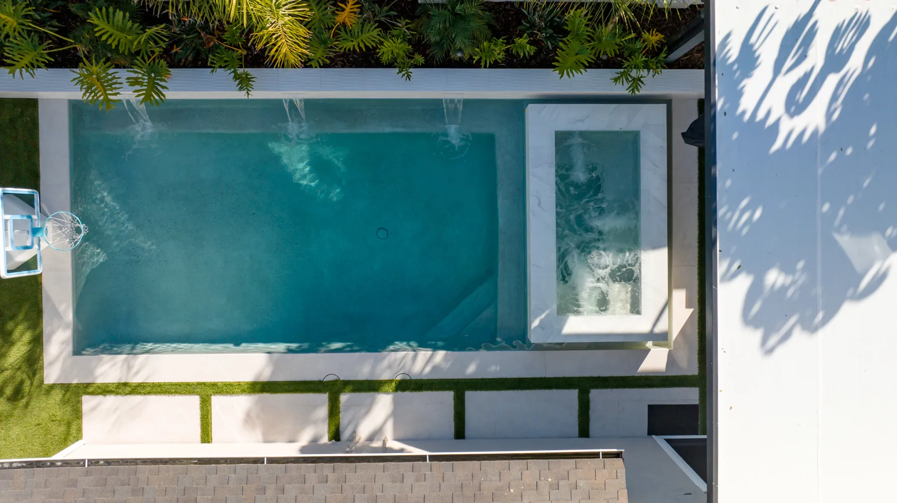 The whole yard from above, the spa set into the corner of the pool and planting running along the white boundary wall.