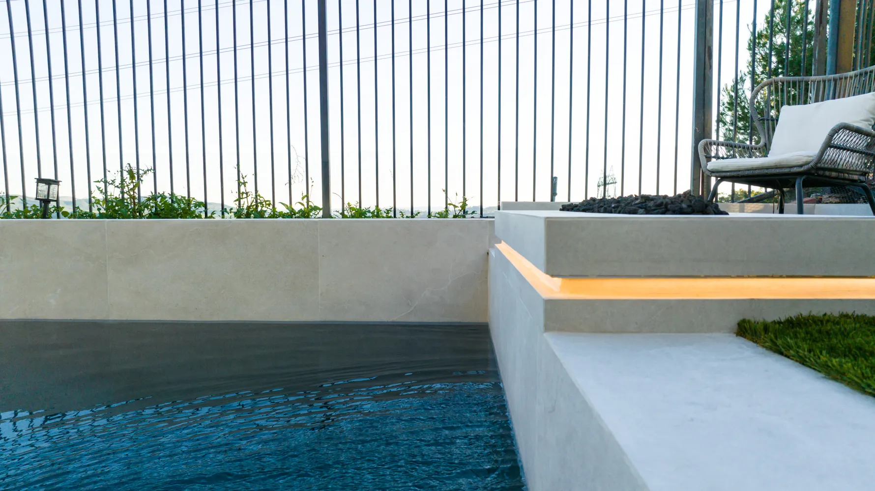 A raised bench lit from underneath along the poolside, its light catching the still, near-black surface.