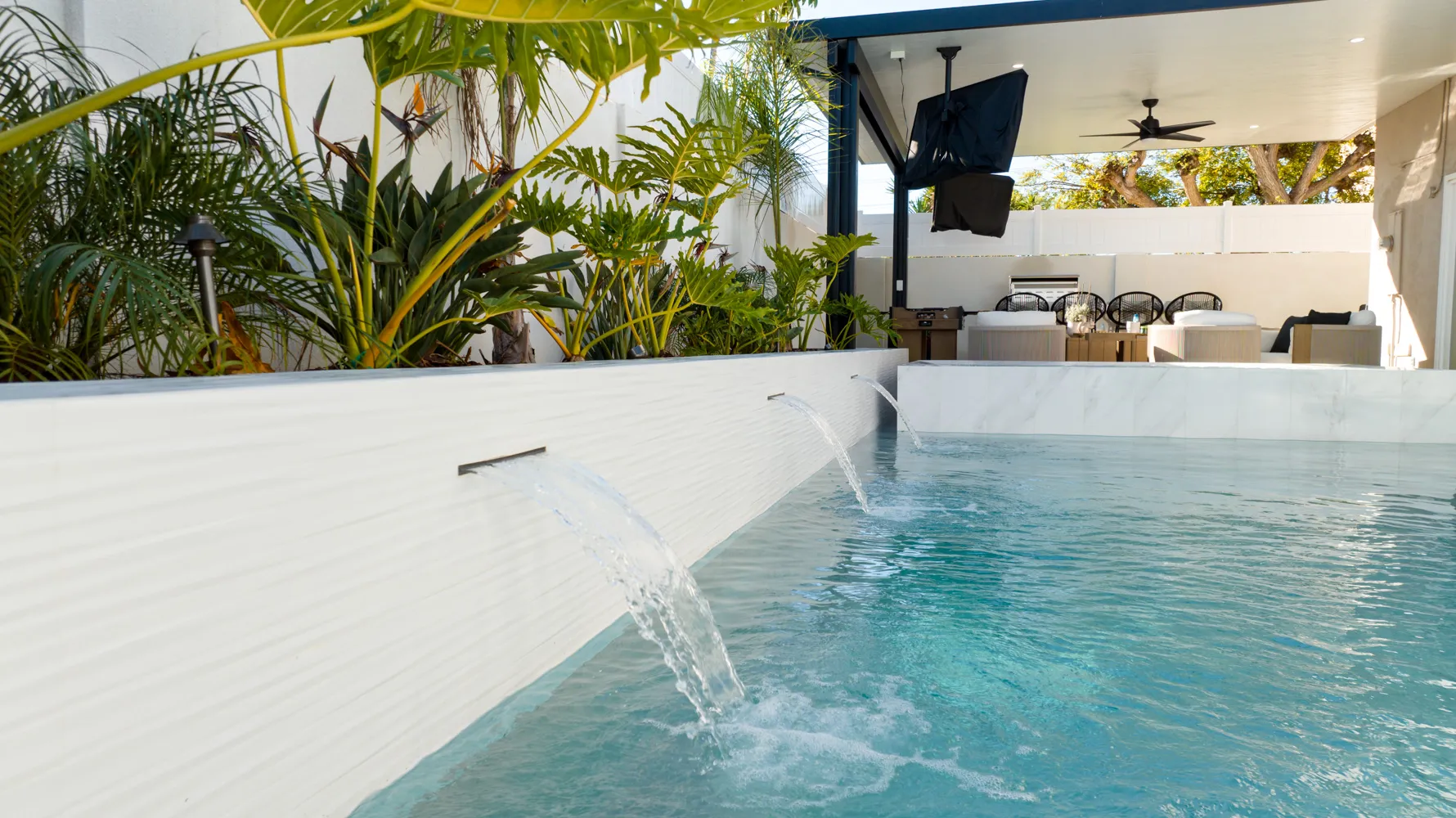A single deck jet arcing into aqua water against a white wall, with palms overhead and a covered seating area at the far end.