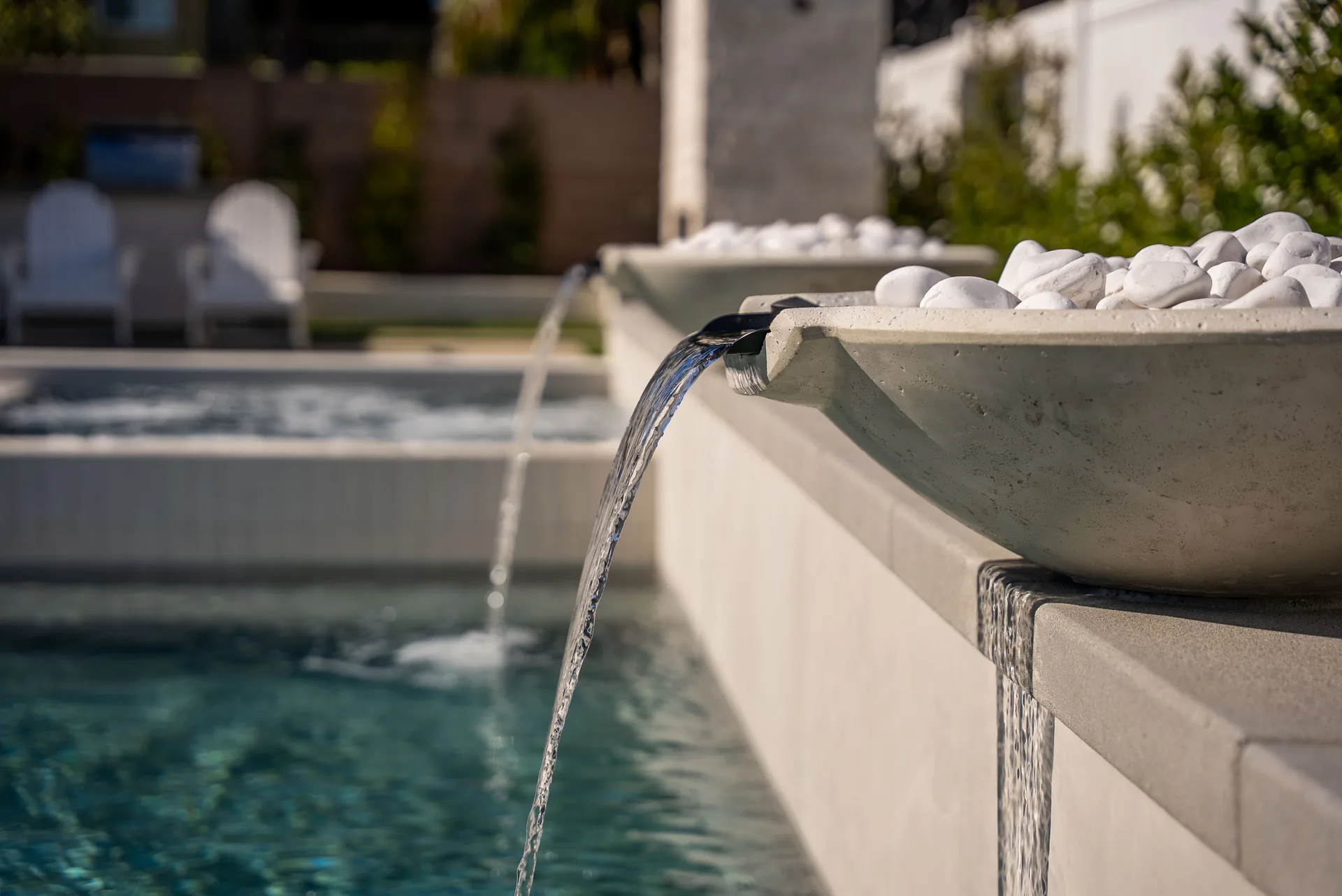A concrete water bowl filled with white stones, pouring a clear spout into the shallow end.