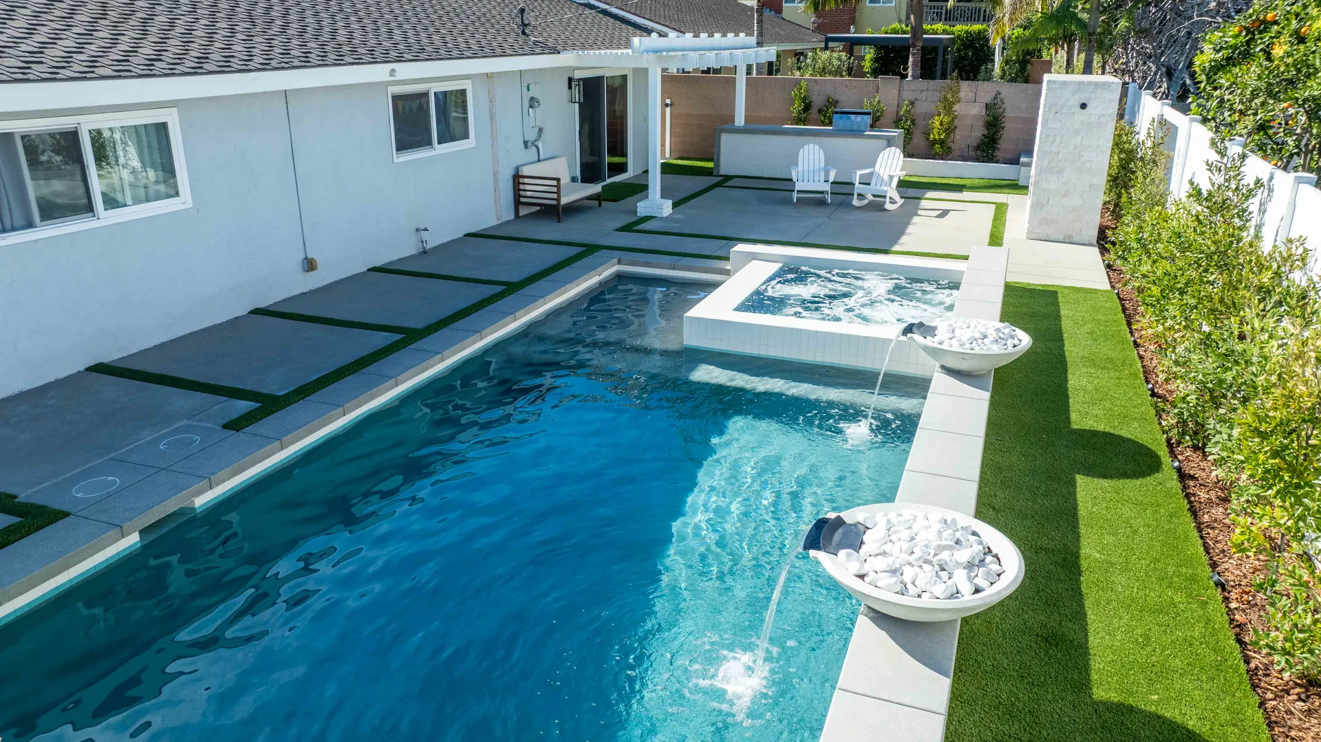 Looking down the pool from the house, with a raised spa, a strip of turf along one flank and a fire bowl set into the deck.
