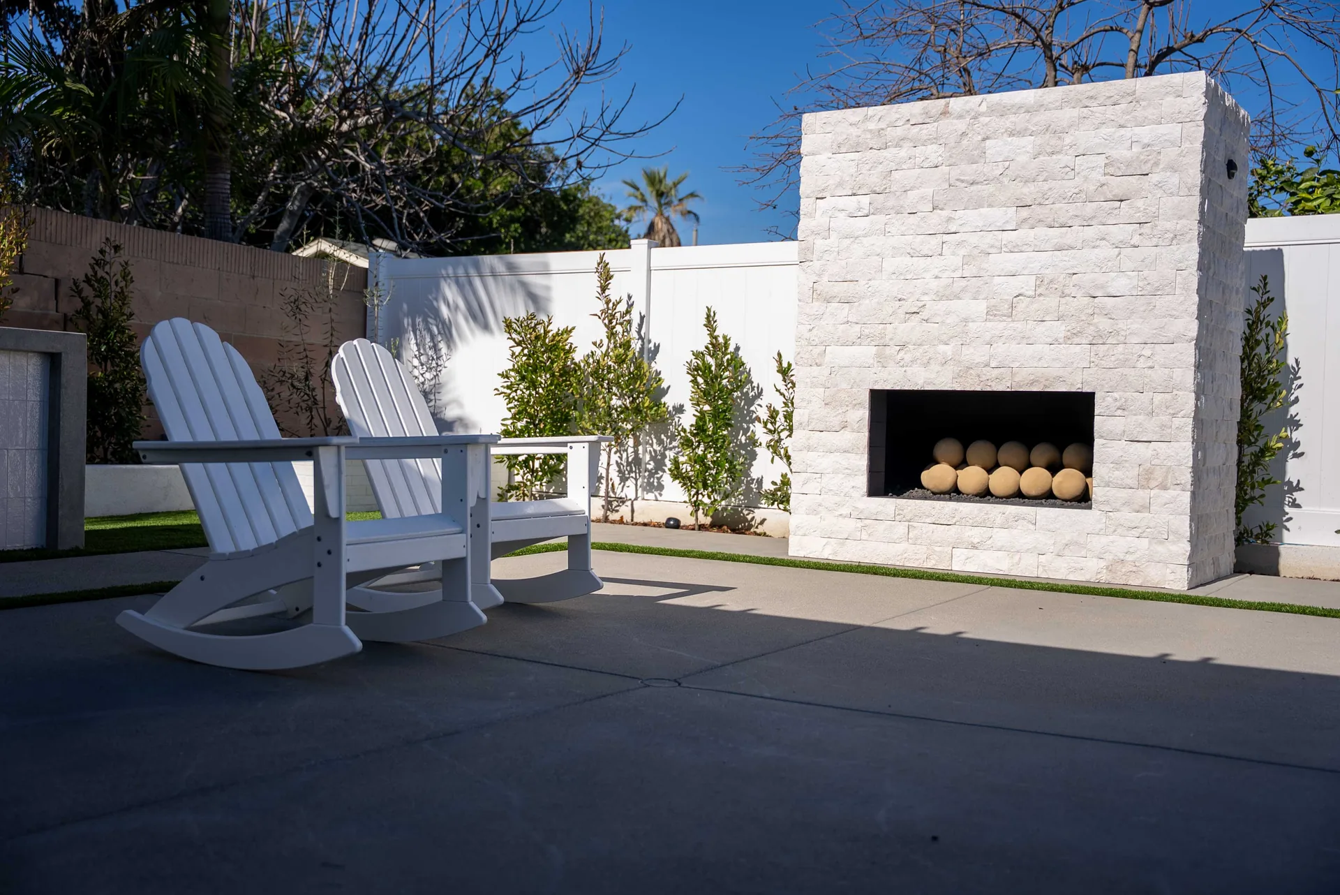 Two white Adirondack chairs turned toward a stacked-stone fireplace holding a row of ceramic spheres.