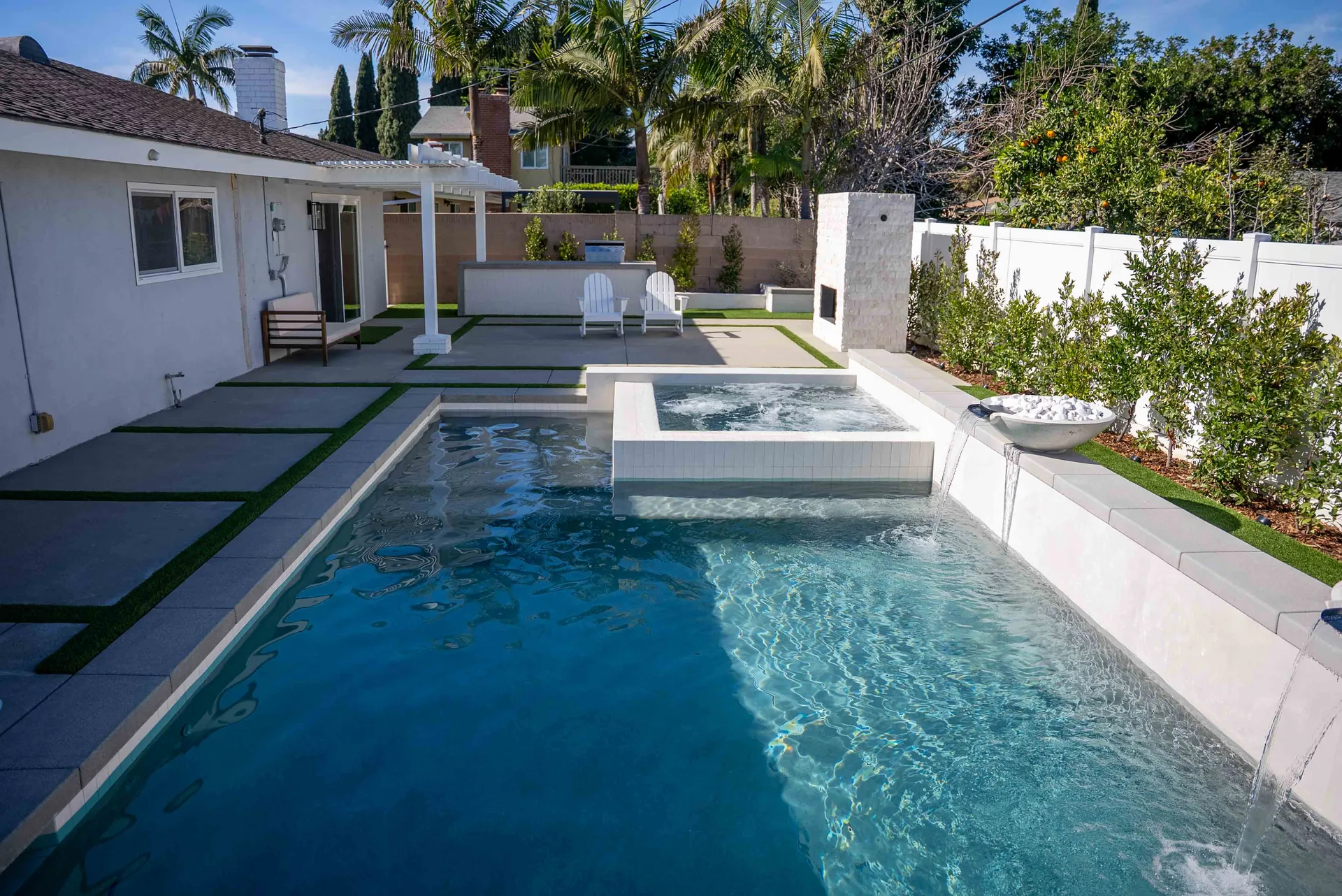 The pool from the covered patio, spa at the far end, deck chairs and planting along the boundary.
