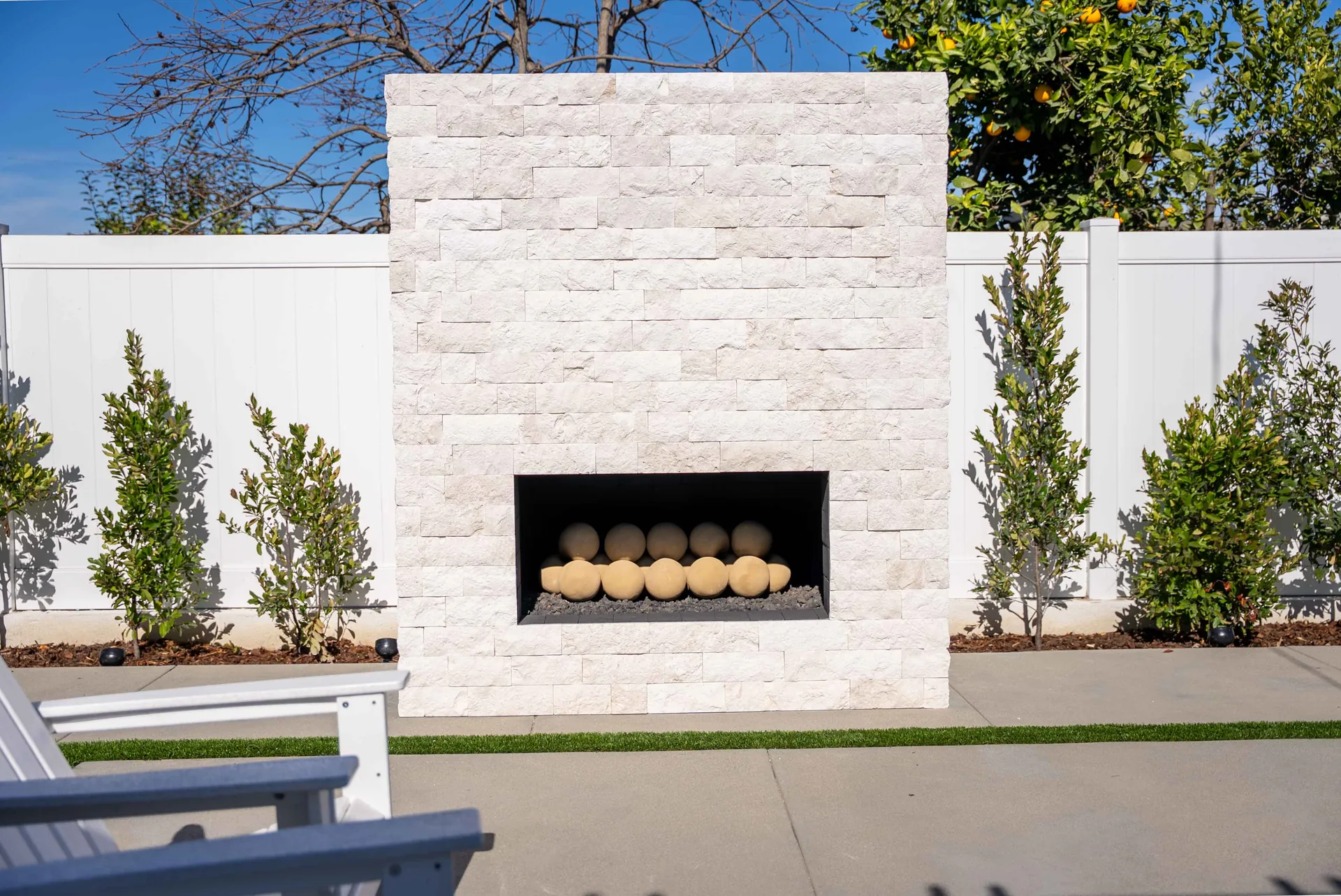 The stacked-stone fireplace unlit in daylight, its firebox filled with pale ceramic spheres.
