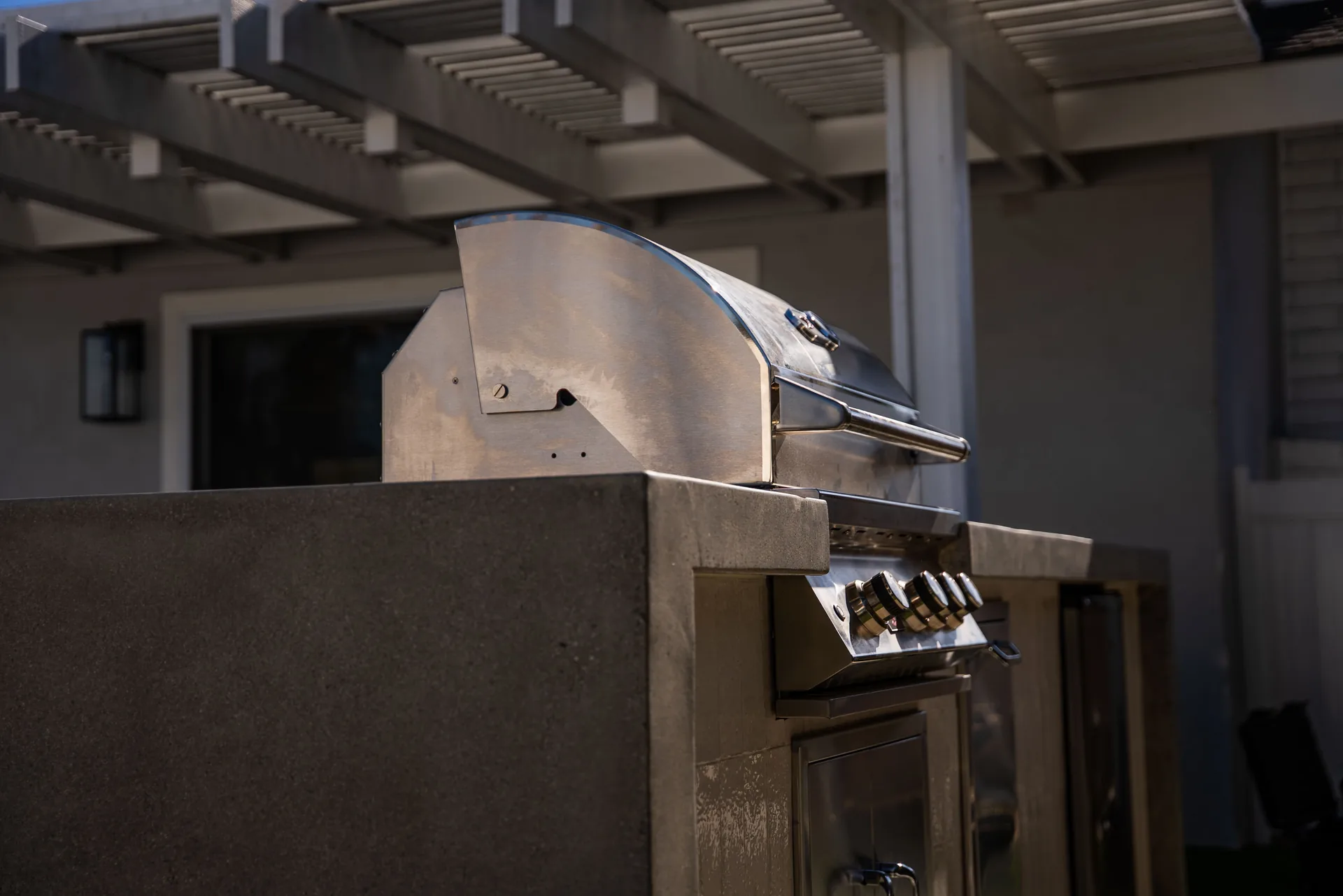 The built-in grill under the patio cover, lid raised, set into a poured concrete counter.
