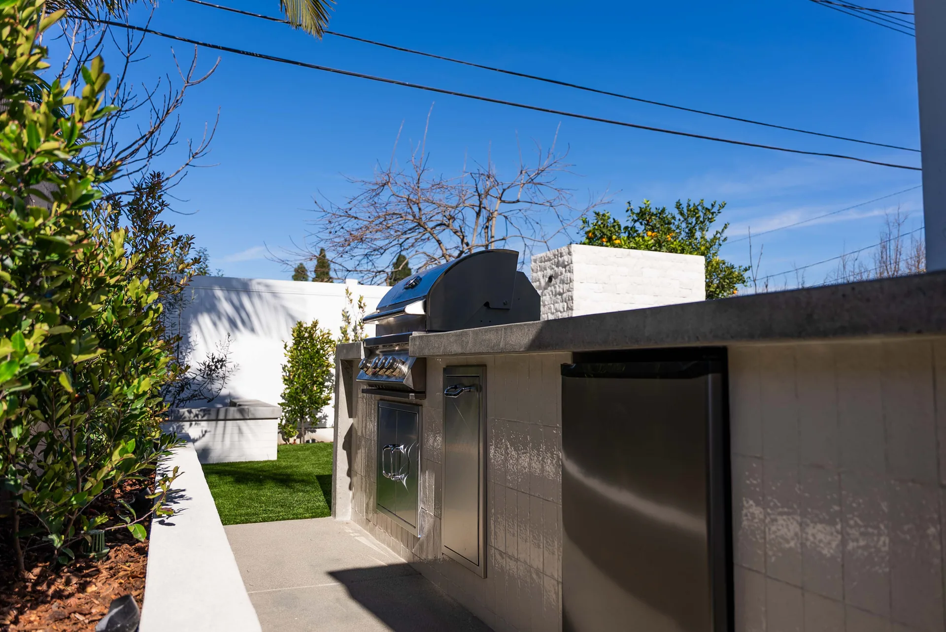 The outdoor kitchen run along the side yard, stainless doors set into a rendered cabinet.