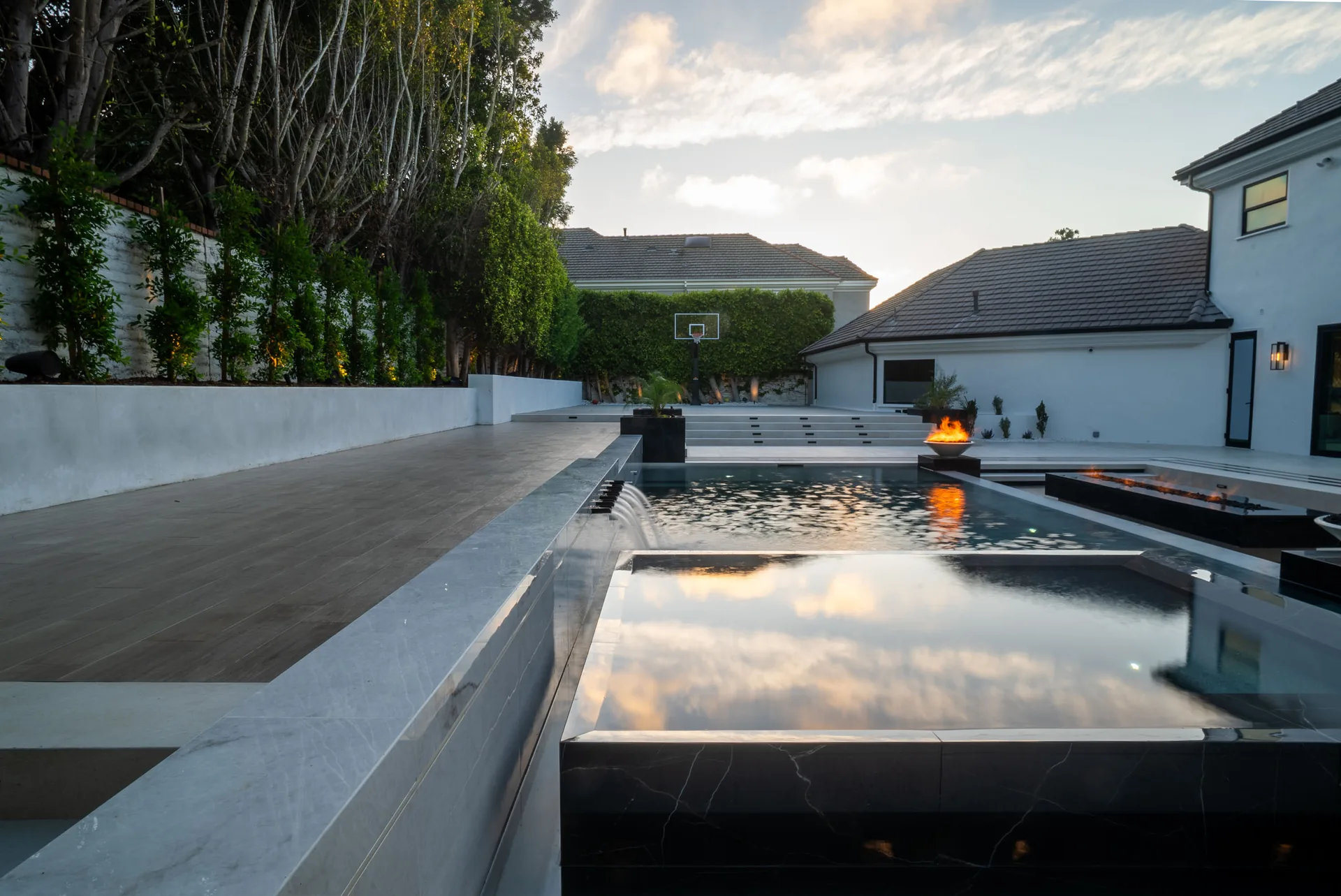 The pool holding a mirror-still surface, black marble coping along the near edge and the house reflected across the water.