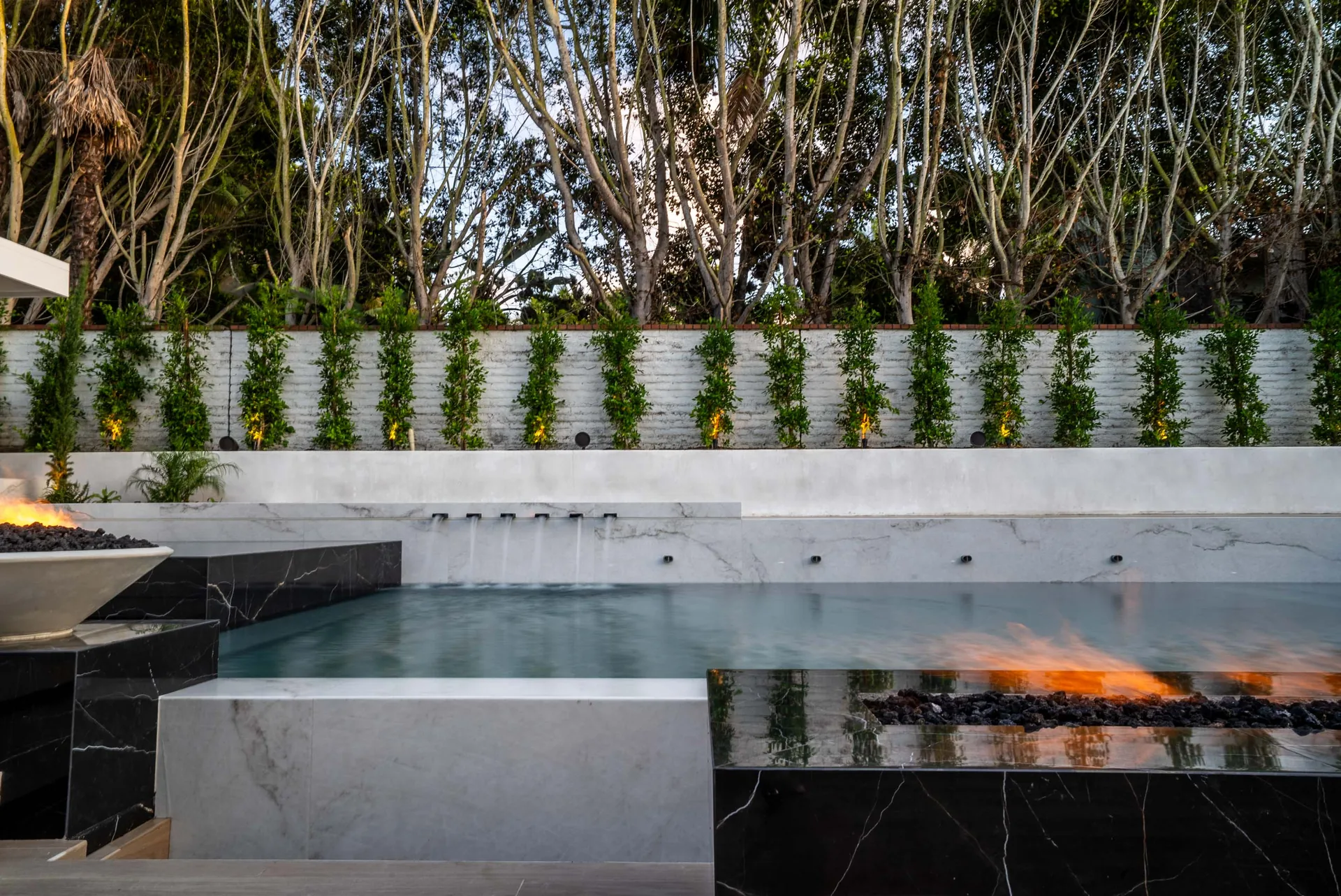 A long fire trough burning at the water's edge, scuppers spilling from a white marble wall into the dark pool.