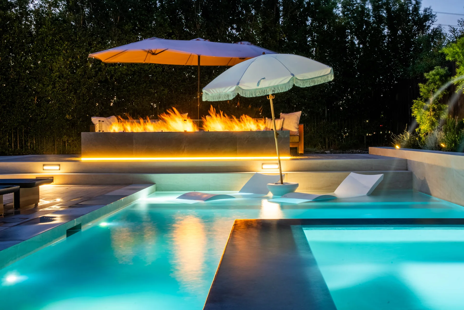 A long line of flame along the raised wall reflected across the lit pool, parasols standing over the tanning shelf.