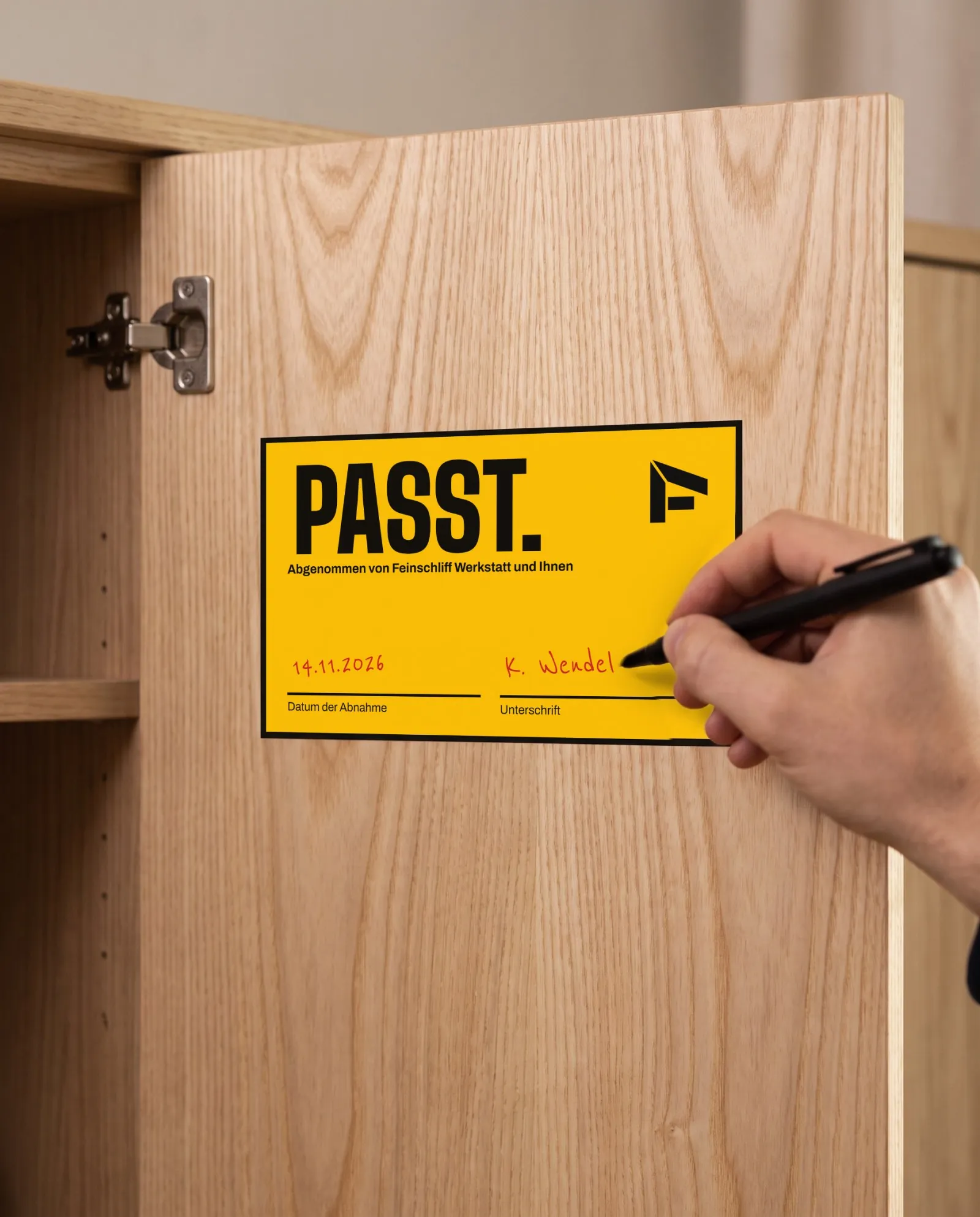 Ein gelbes Etikett „Passt.“ mit Datum und Unterschrift in einer Schranktür