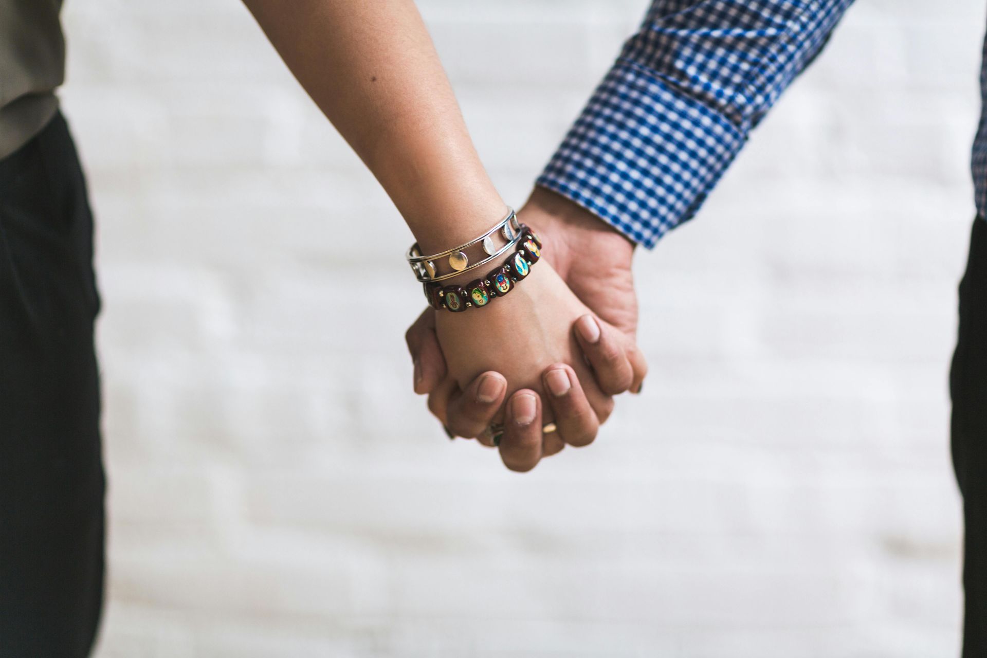 Two people holding hands, one in a blue checkered shirt, against a blurred light background