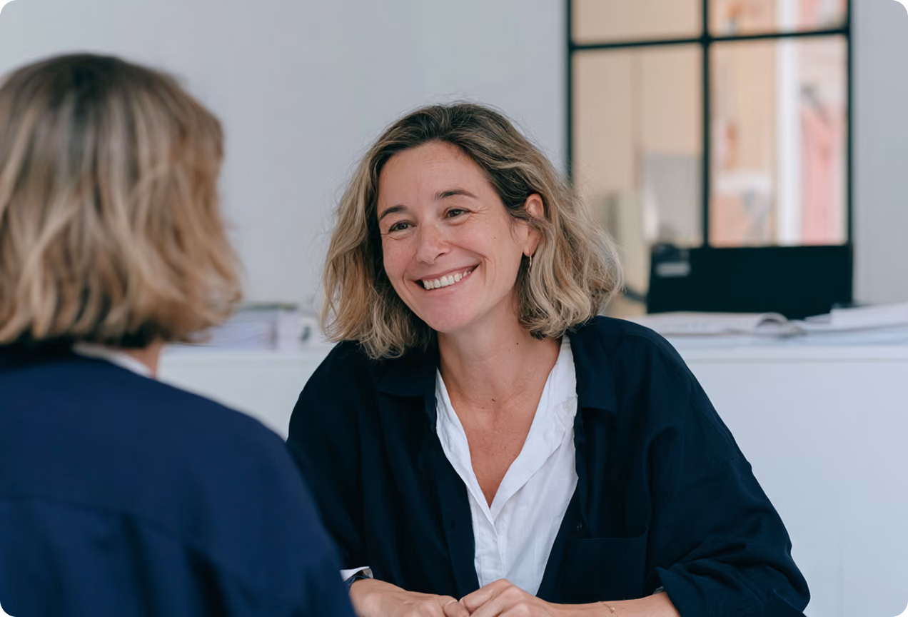 Deux femmes assises face à face dans un bureau, l'une souriant chaleureusement à l'autre.