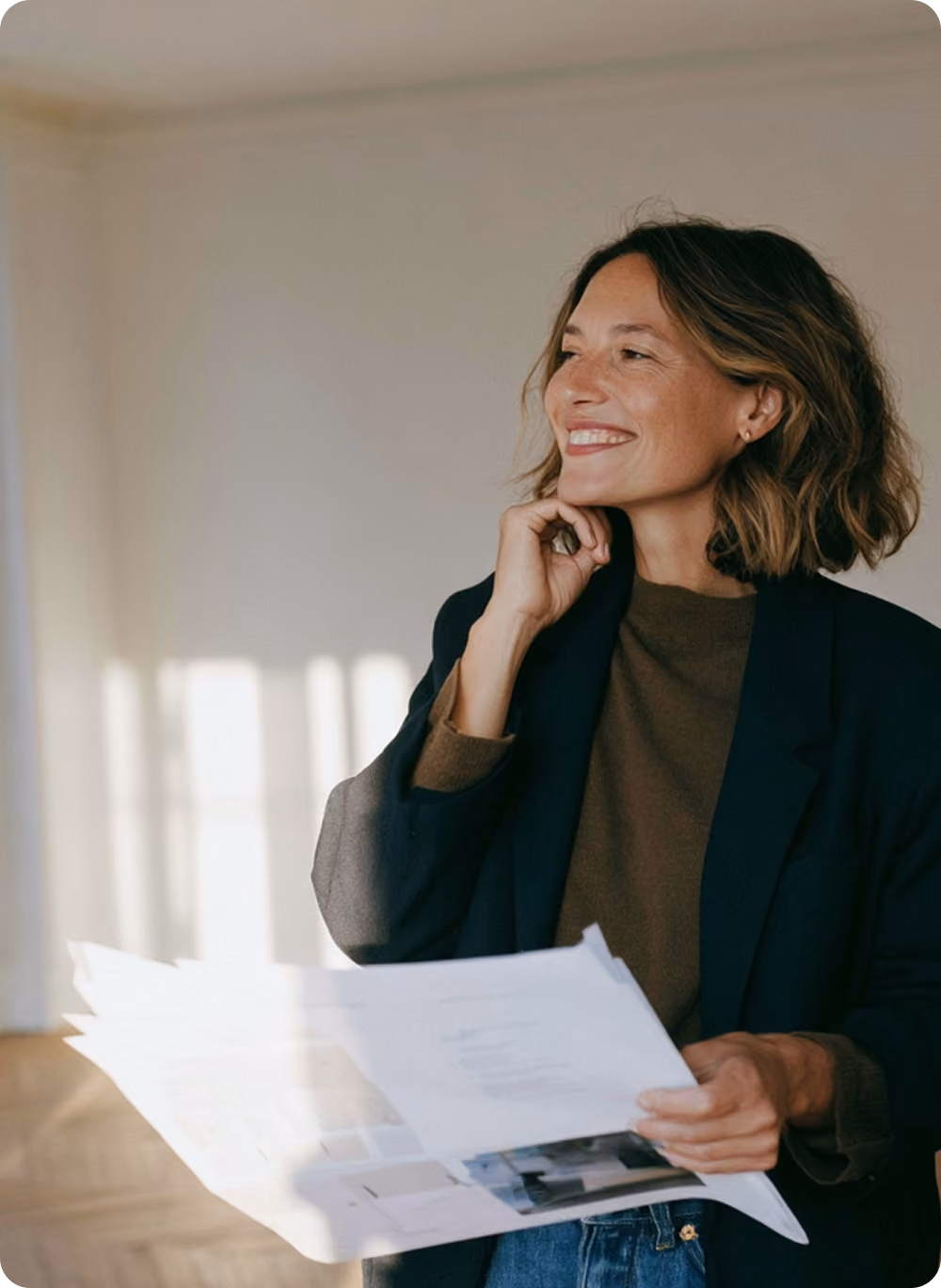 Femme souriante tenant un document dans une pièce lumineuse, regardant sur le côté.