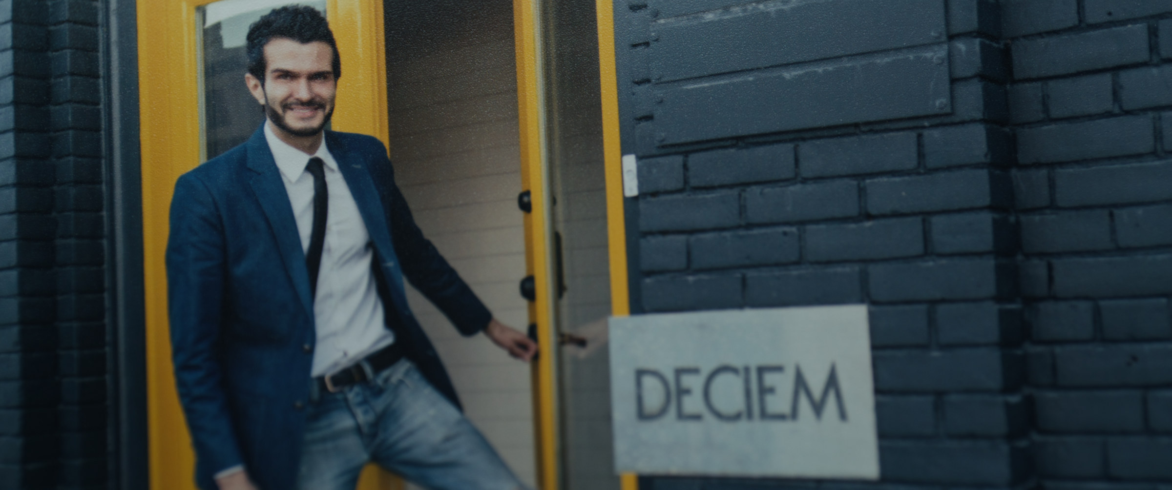The Abnormal Beauty Company: archival photo of a smiling man in a suit opening a door beside a DECIEM sign