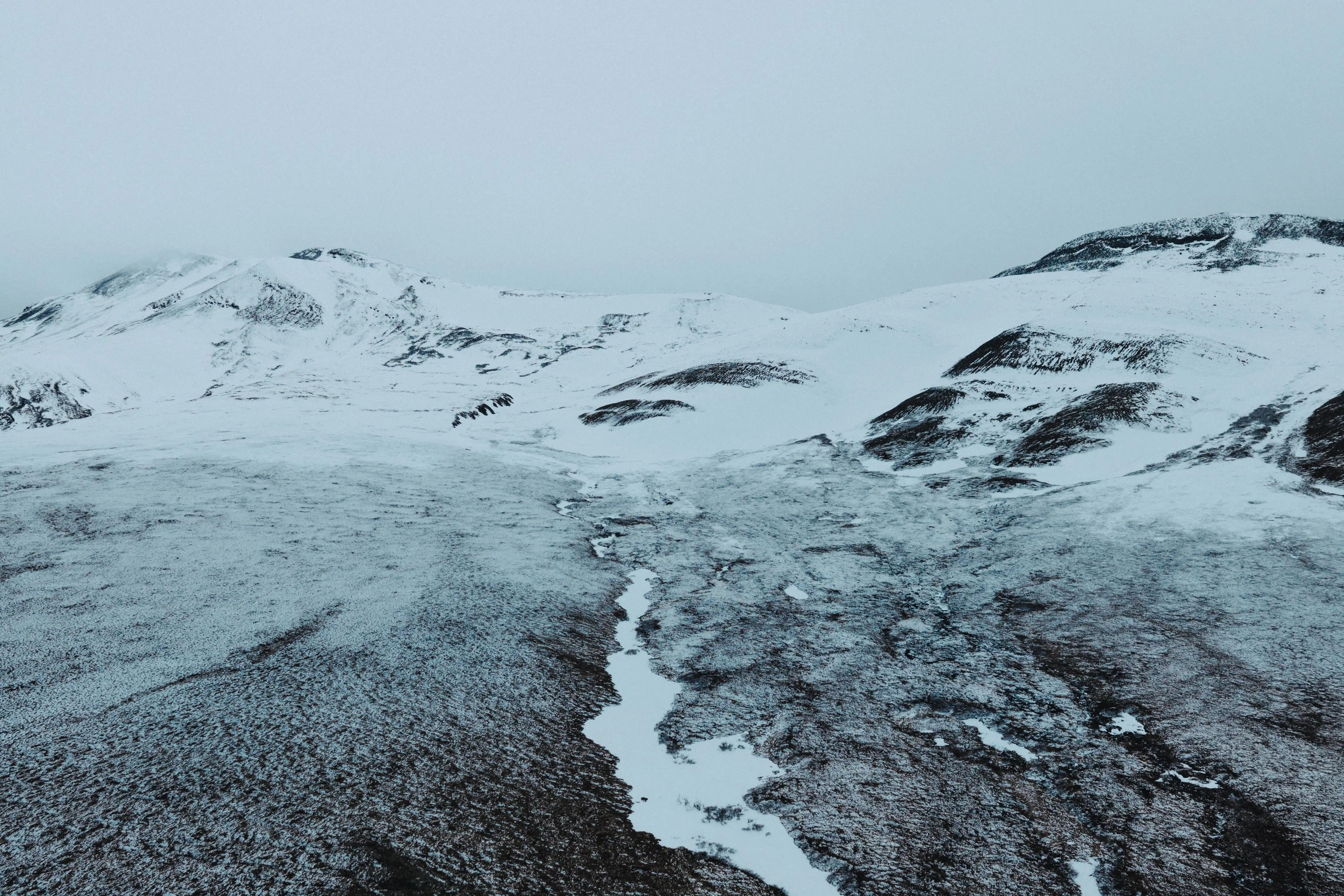 Aerial view of a snow-covered ridge and tundra under overcast light