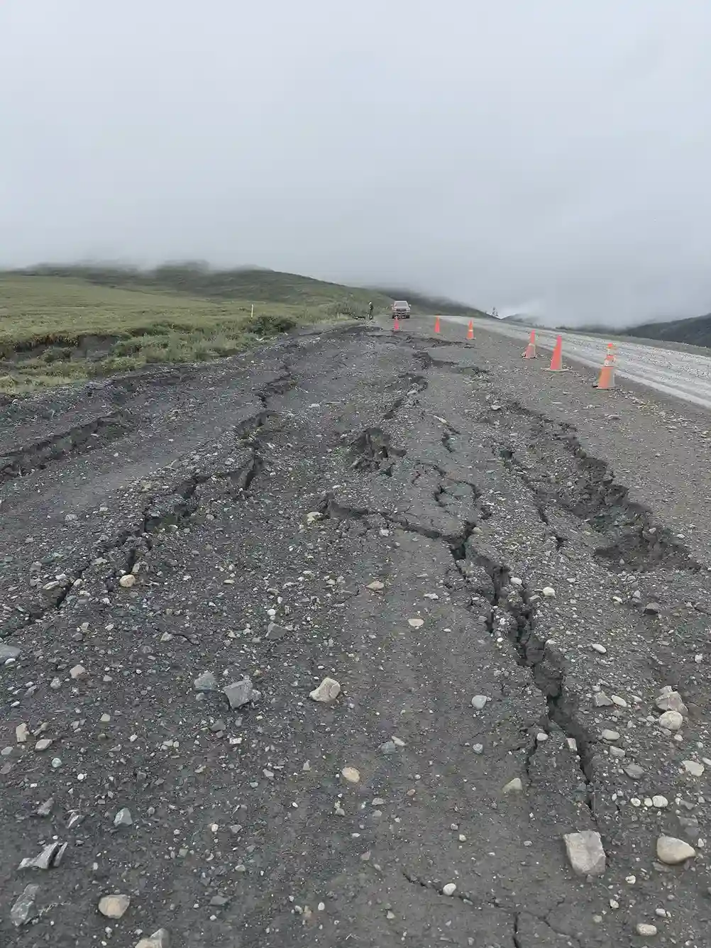 Cracked and subsiding gravel highway marked with traffic cones where permafrost has thawed beneath it