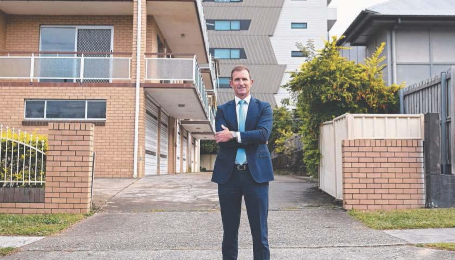 Man in a suit standing in the driveway of a brick unit block