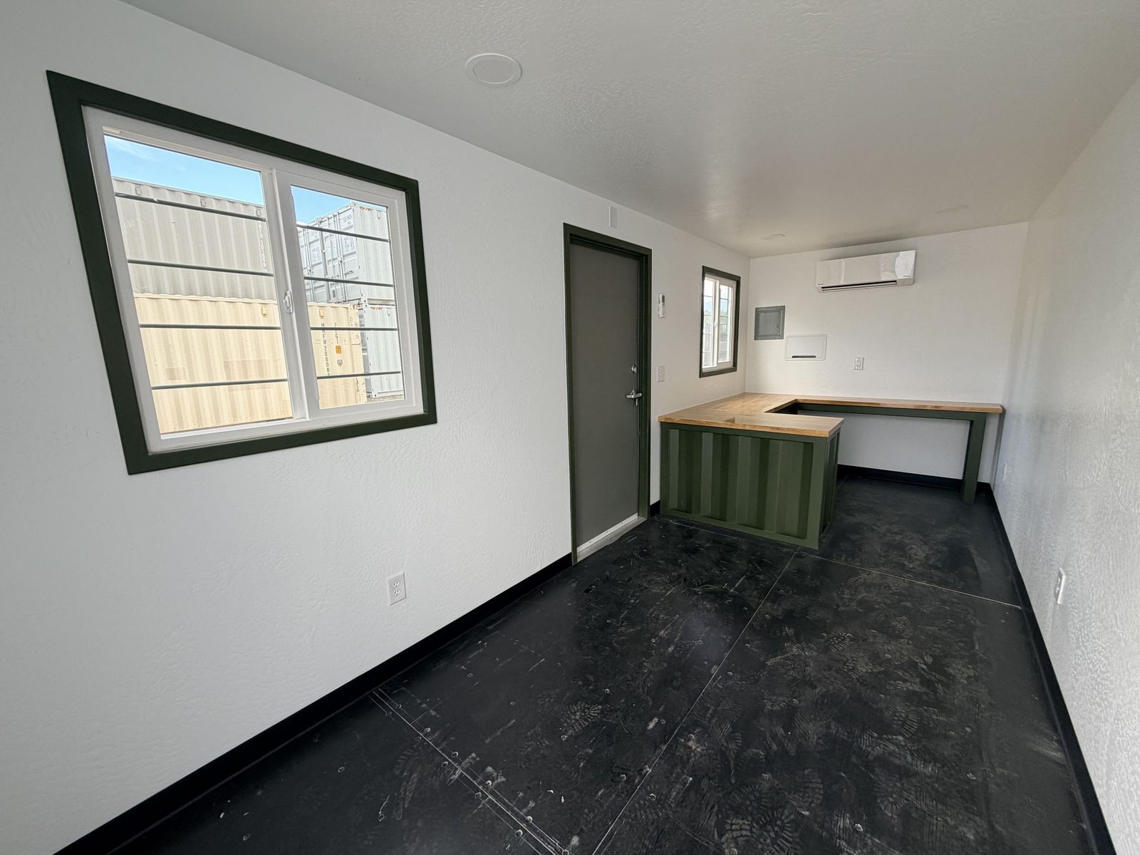Container office interior with an L-shaped slate reception counter, wood top, and a personnel door