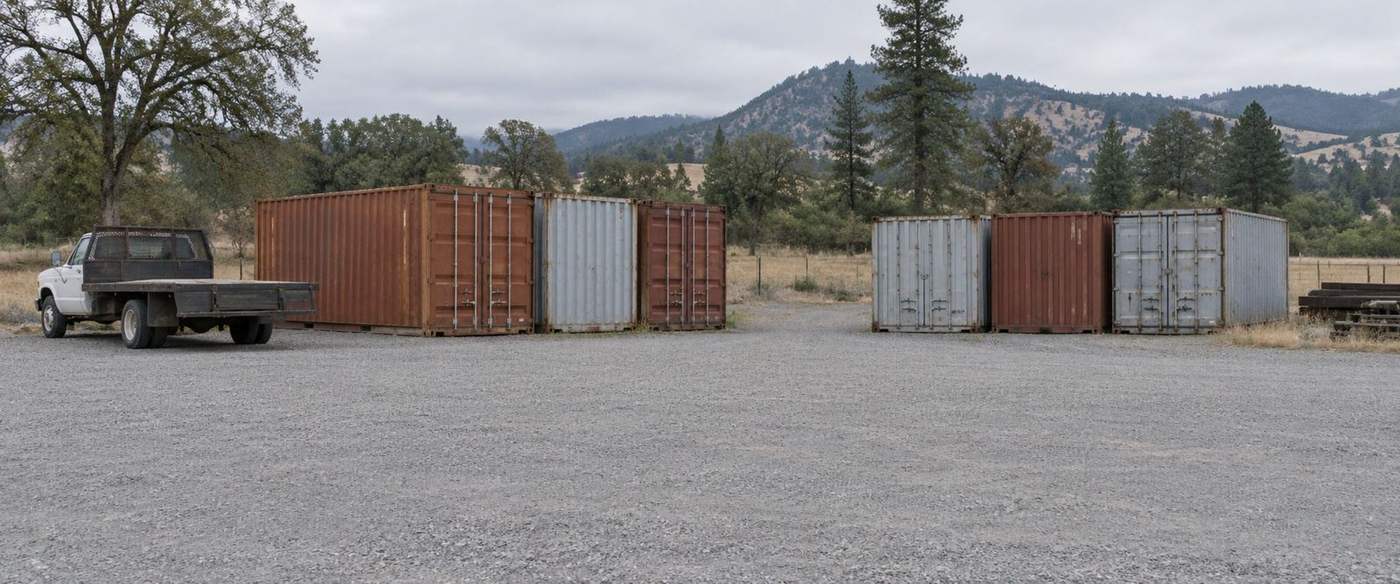 The first Medford yard in 2012, weathered rust and galvanized containers on gravel with an old flatbed truck, Rogue Valley hills behind