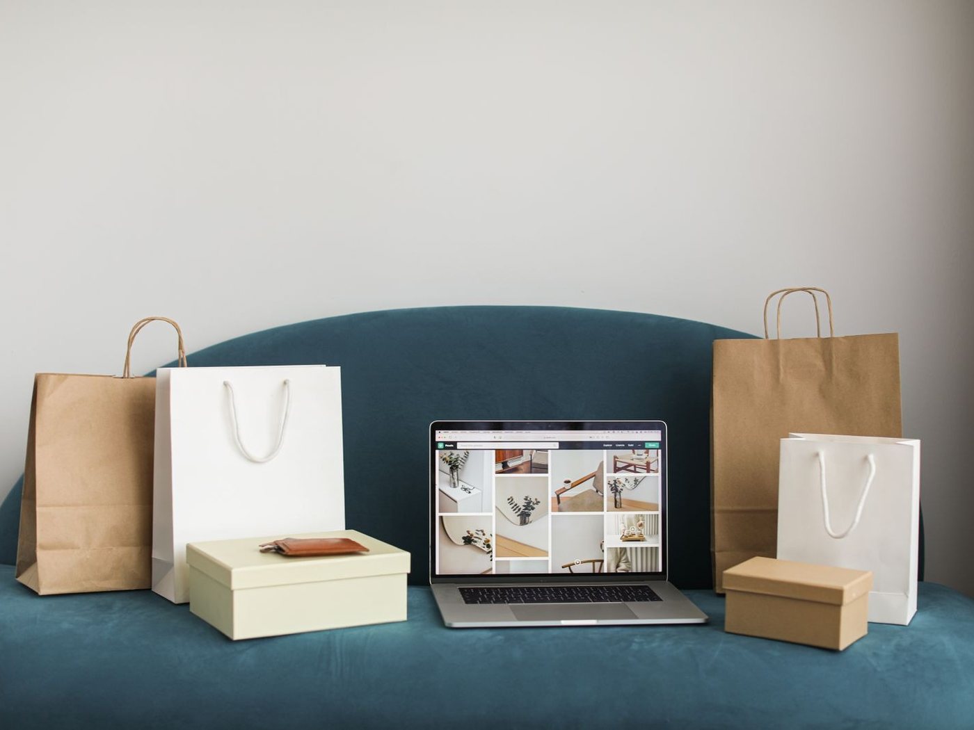 A laptop open on an online store, with paper shopping bags and gift boxes on a blue sofa