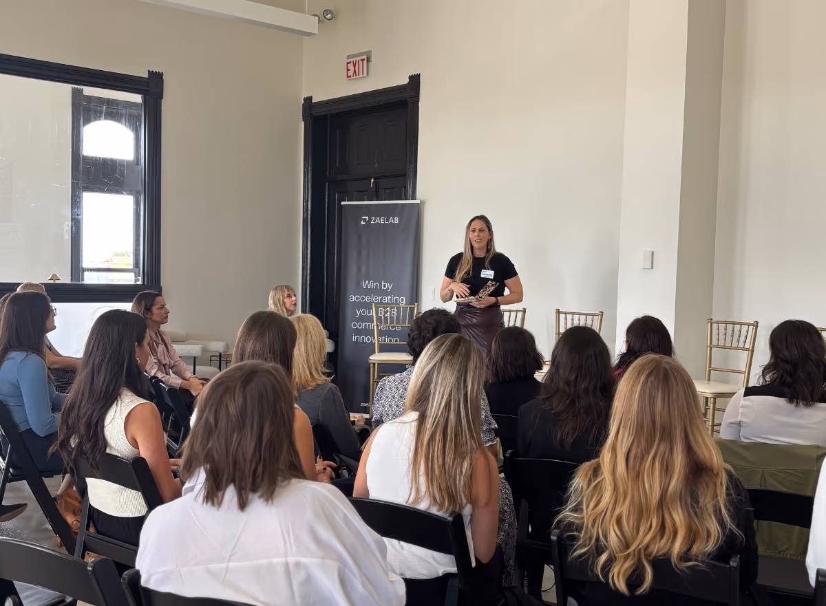 Jennifer Daugherty from Zaelab delivers opening remarks to the audience at the Women in B2B Thought Leadership Collective, with Zaelab and Shopify event banners behind her.