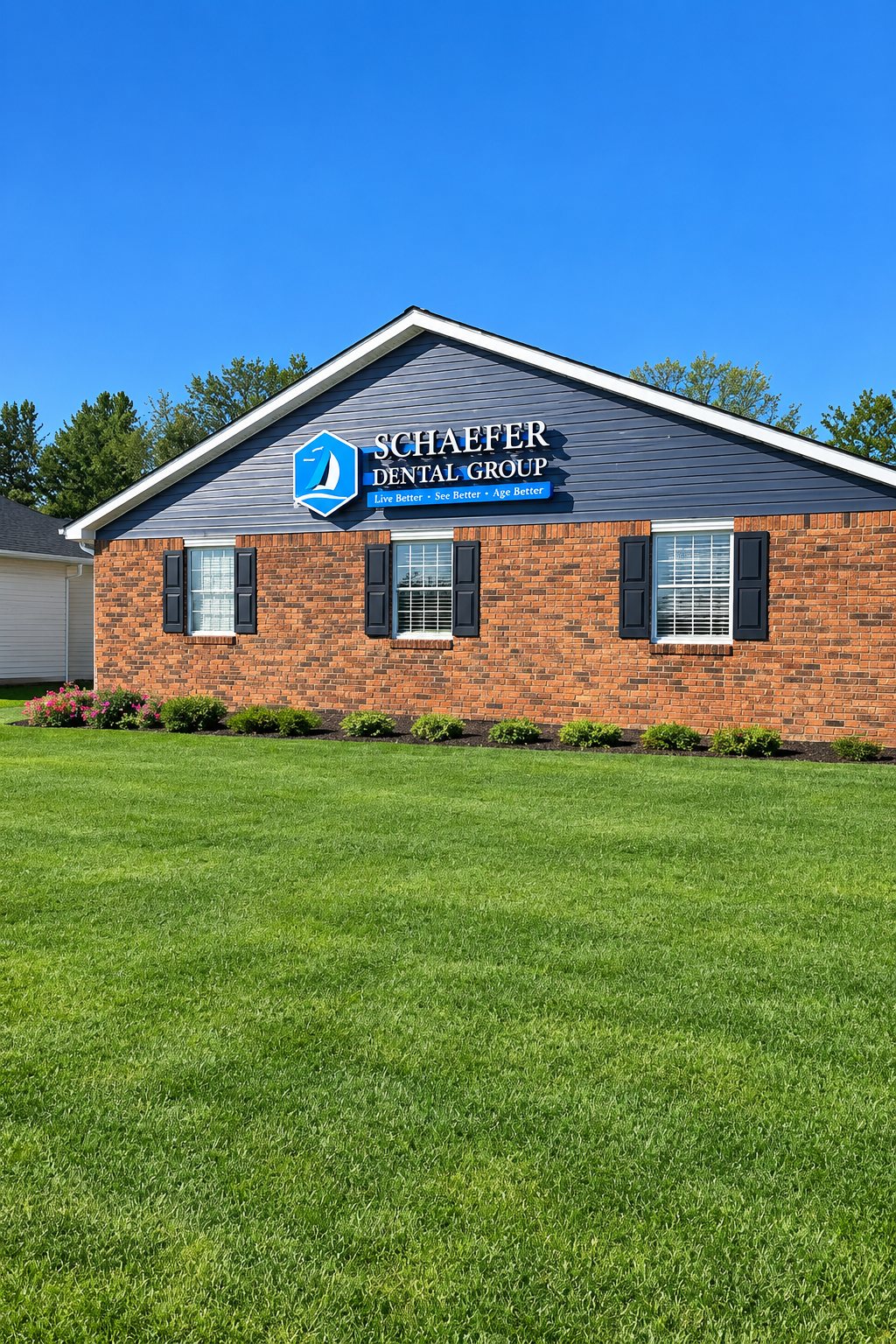 Exterior of Schaefer Dental Group in Brighton, MI, with the office sign above the brick building and lawn.