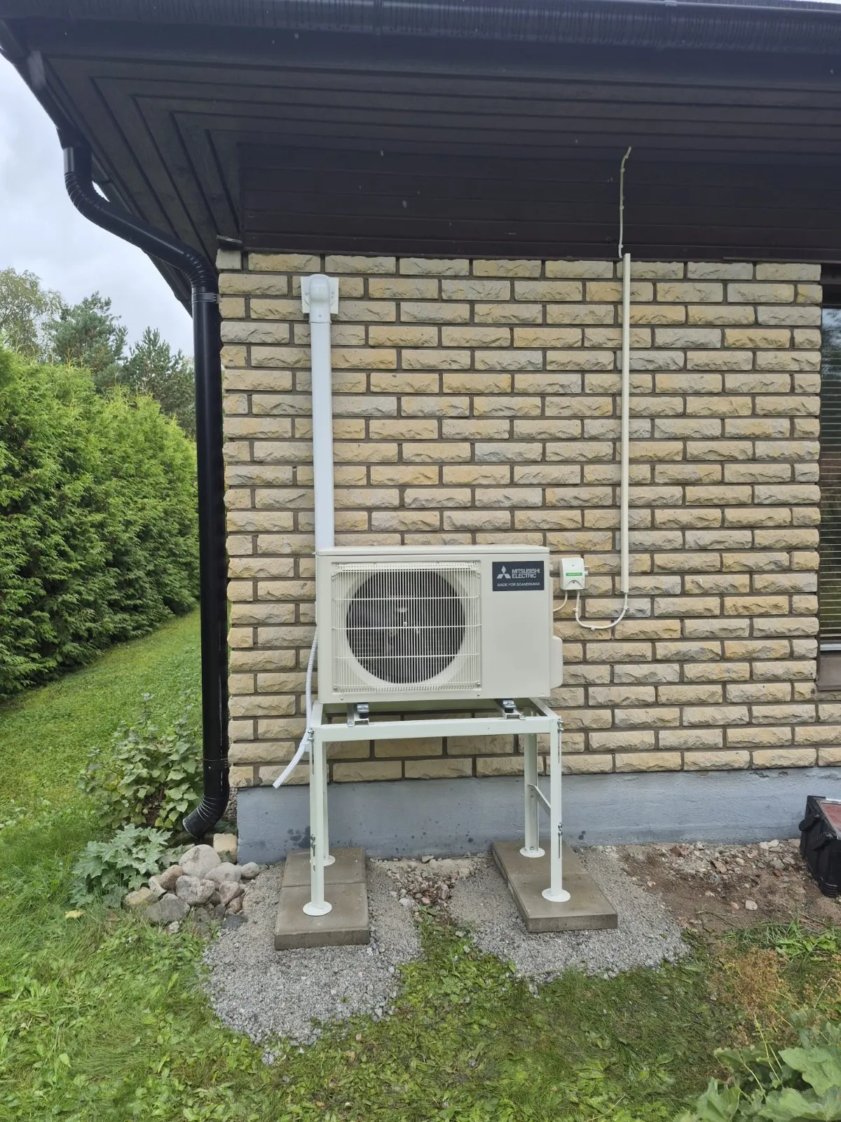 Mitsubishi Electric -ilmalämpöpumpun ulkoyksikkö jalustalla omakotitalon tiiliseinän vieressä