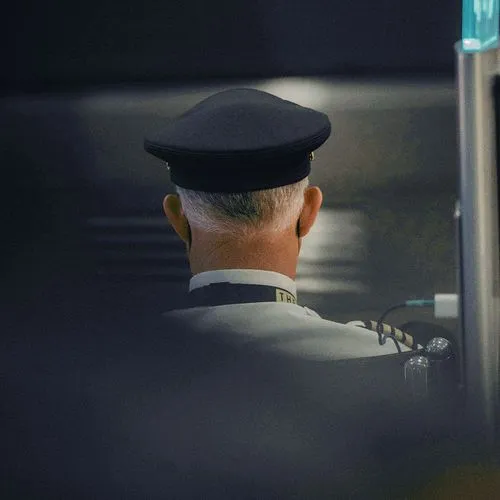 A uniformed airport officer seen from behind at a workstation