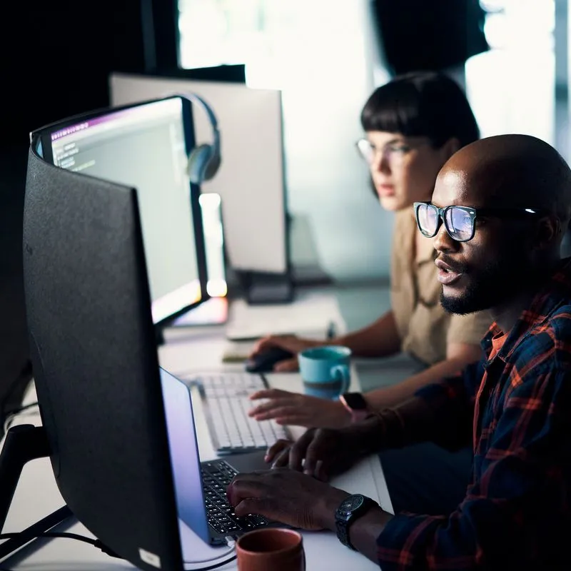 Two colleagues working at computer monitors in a dark office