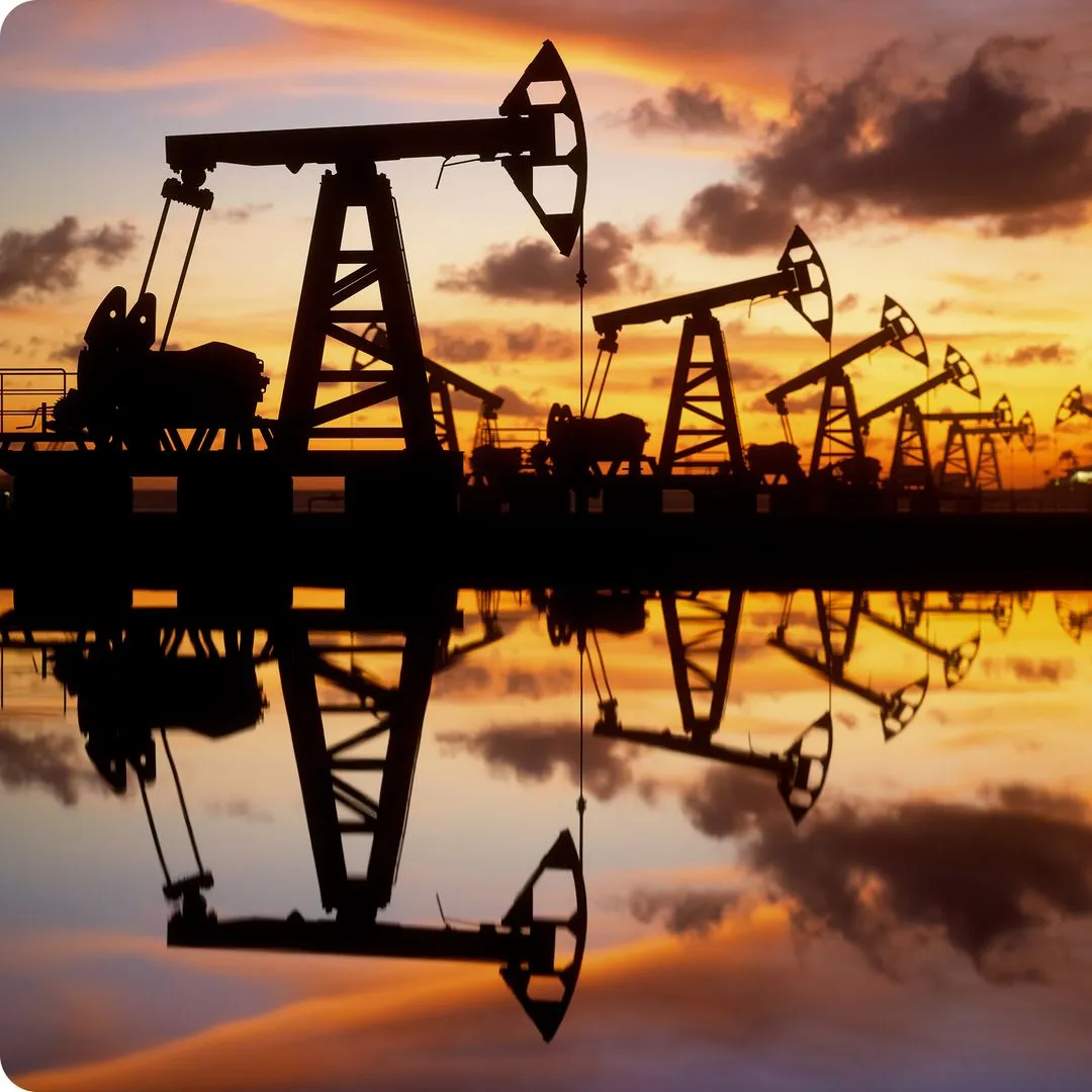 Silhouetted oil pumpjacks reflected in water at sunset