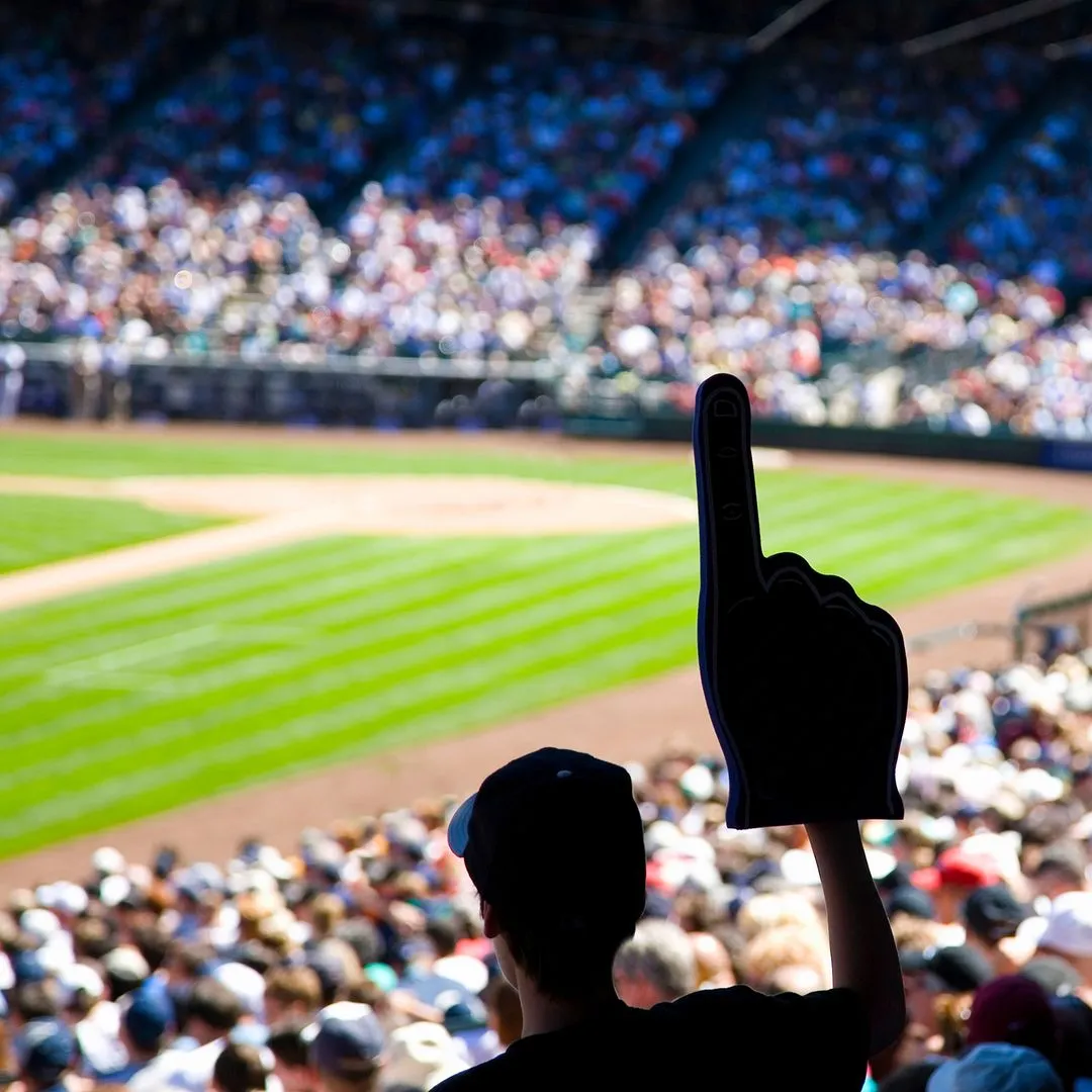A spectator in a baseball stadium raising a foam finger toward the field and crowd