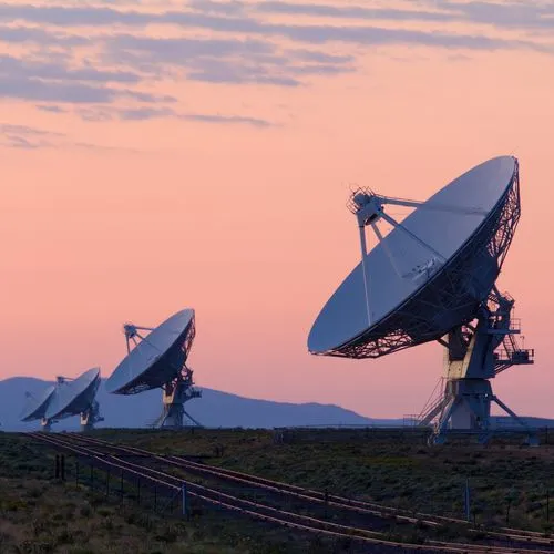 A row of large satellite dishes in an open landscape at dusk