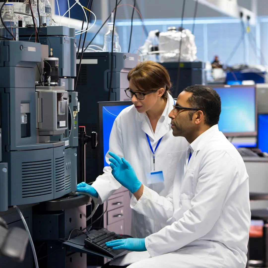 Two researchers in white coats working together at lab equipment