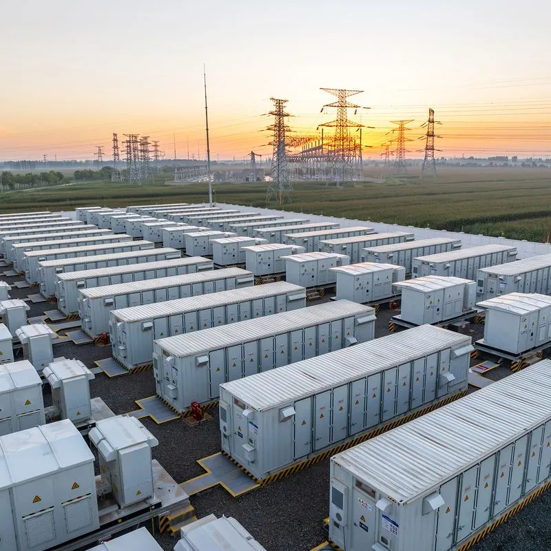 Aerial view of rows of grid substation containers with transmission towers at sunset