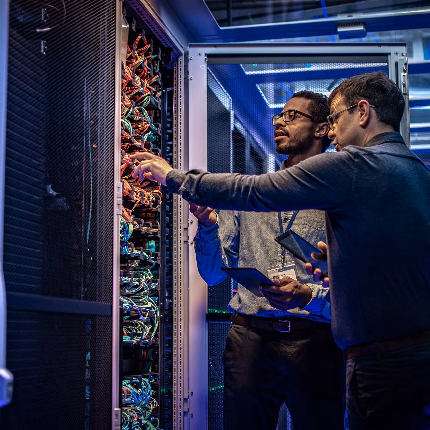 Two technicians inspecting cabling inside a data center server rack
