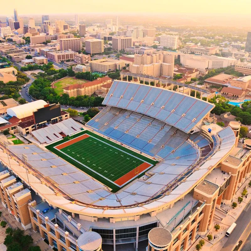 Aerial view of a large university football stadium at sunset with a city skyline behind it