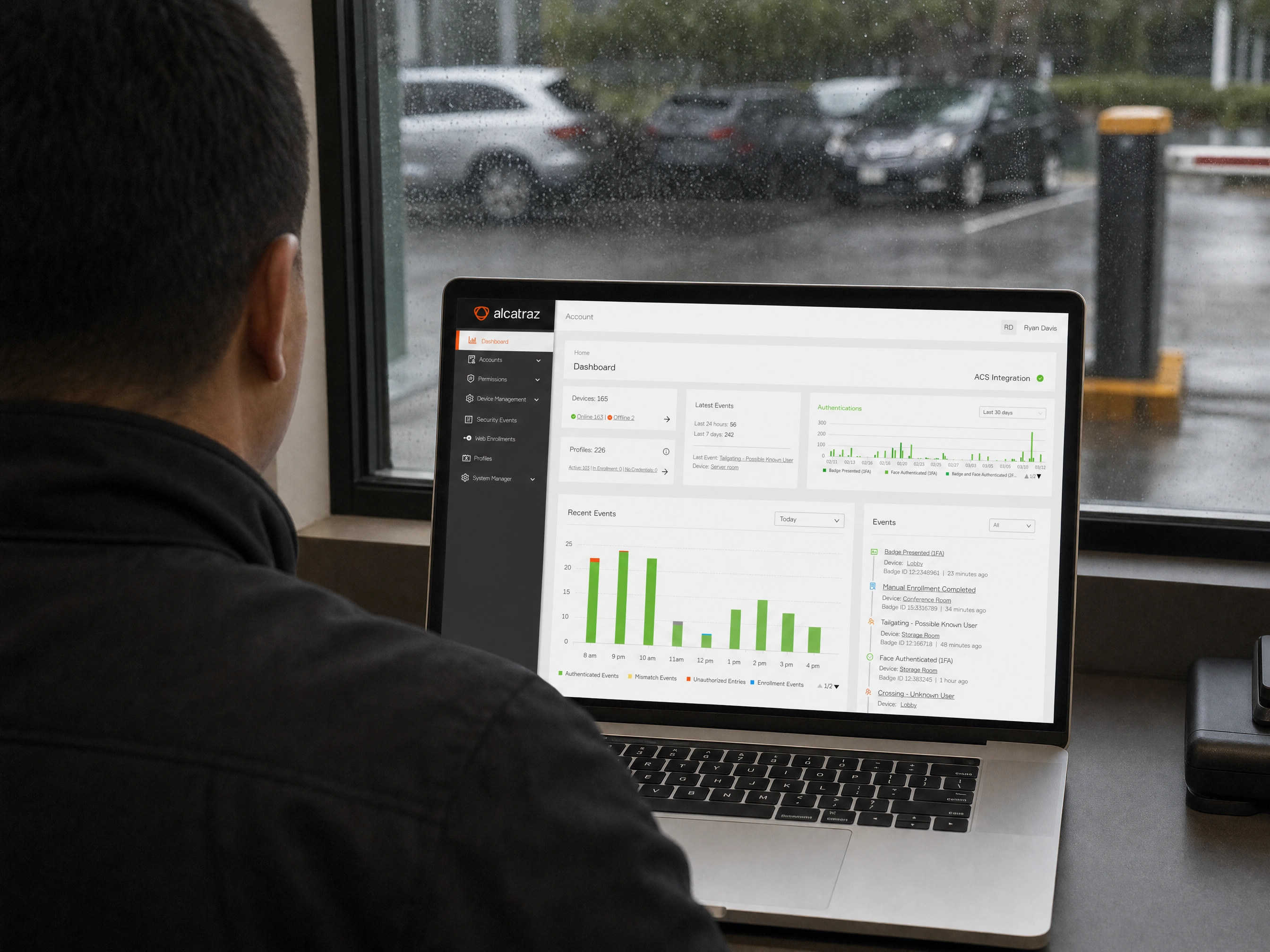 A security operator reviewing the Rock Cortex dashboard on a laptop beside a rain-streaked window overlooking a gated lot