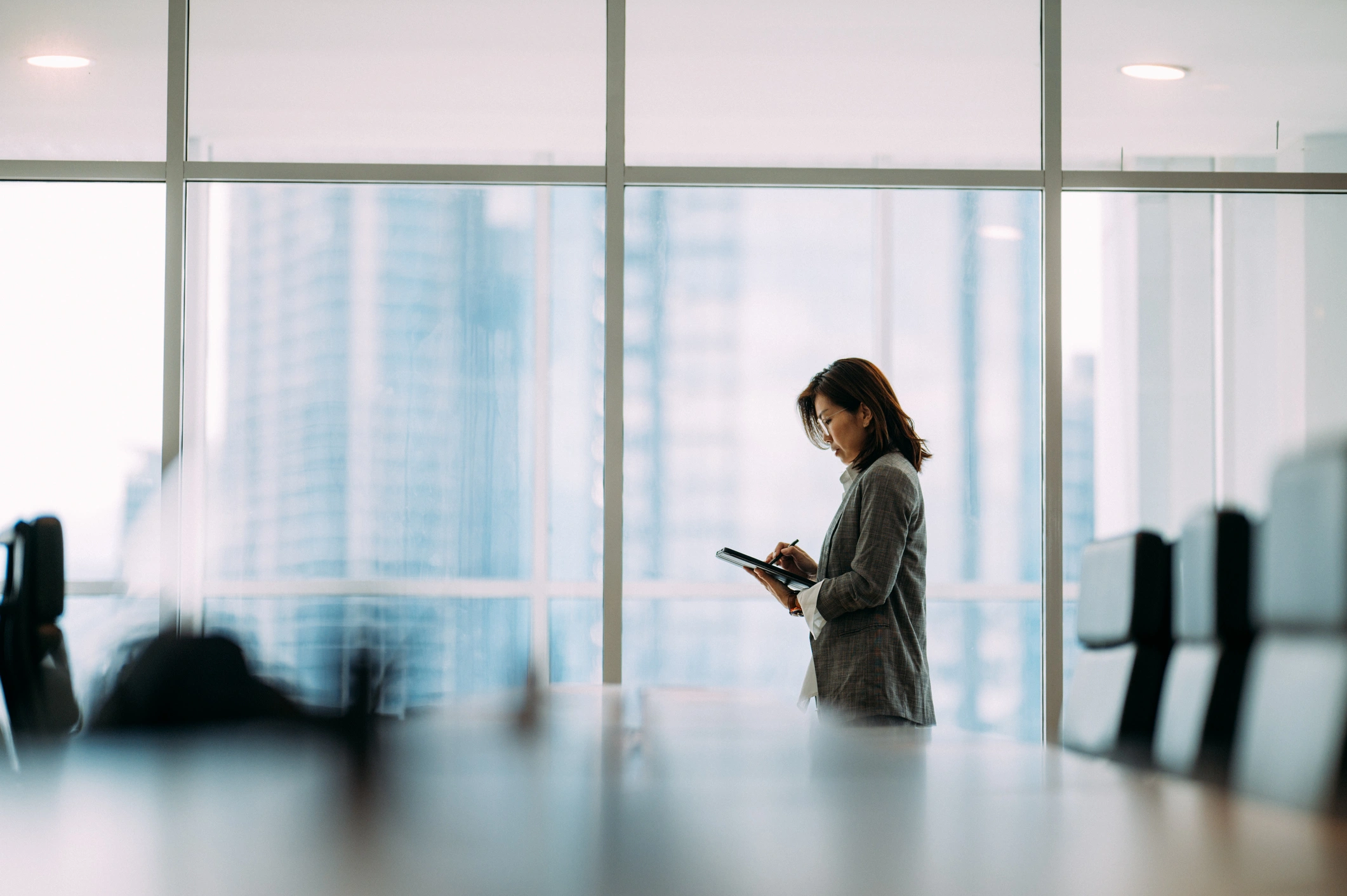 An executive writing on a tablet in a glass-walled boardroom above a city skyline