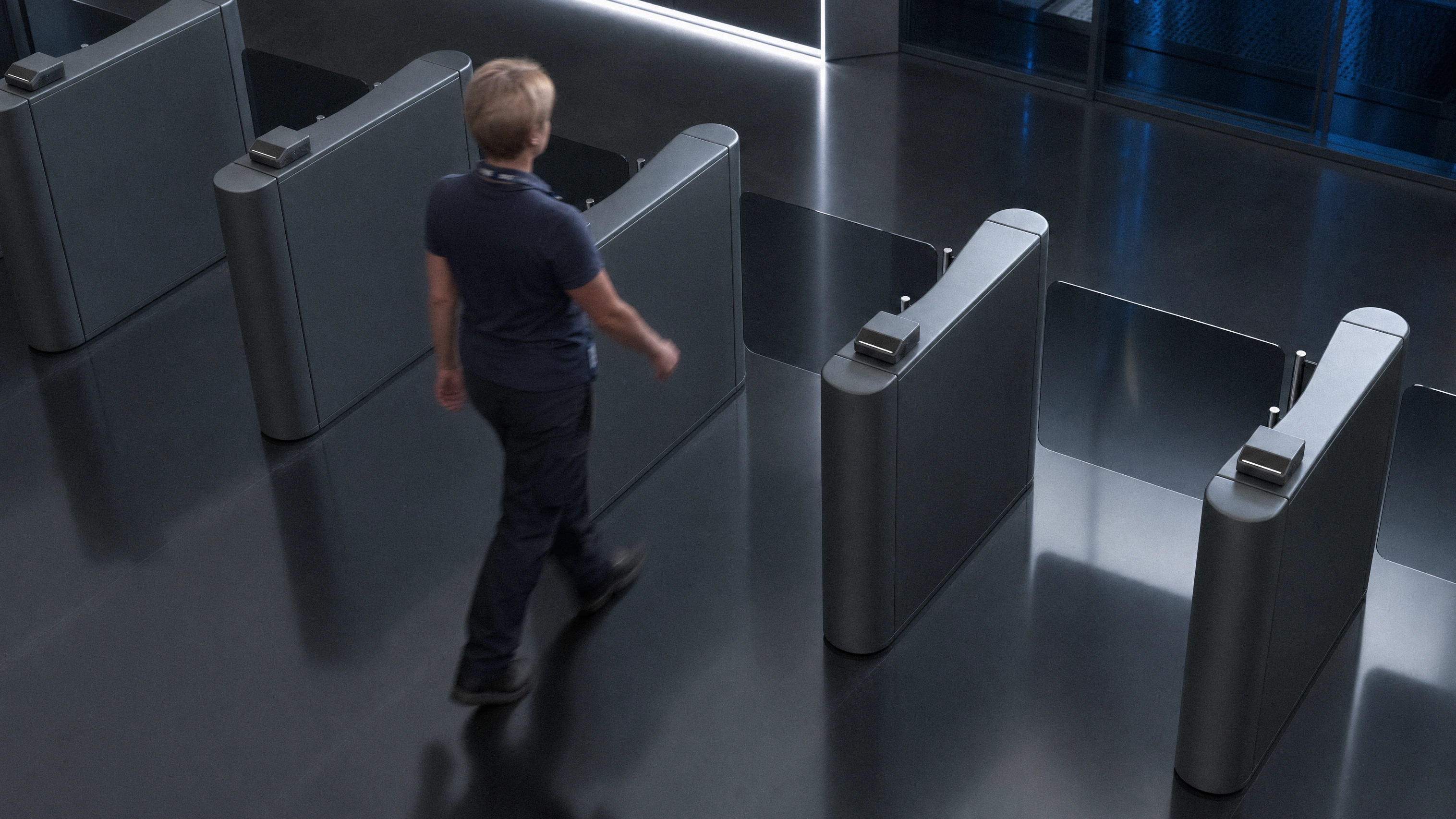 An employee walking through a bank of speed-gate turnstiles in a corporate lobby without stopping