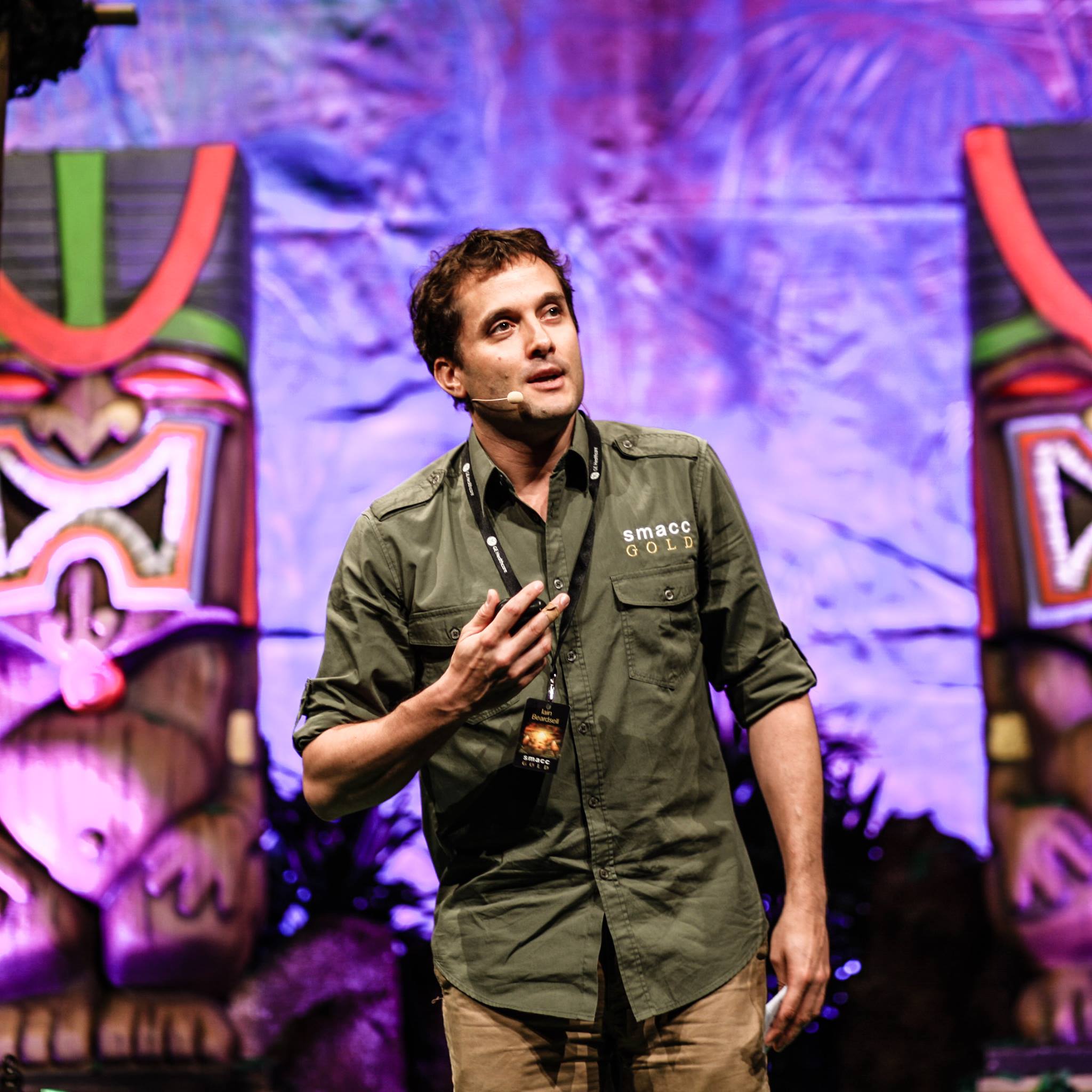 Iain Beardsell speaking on stage at SMACC, wearing a headset microphone