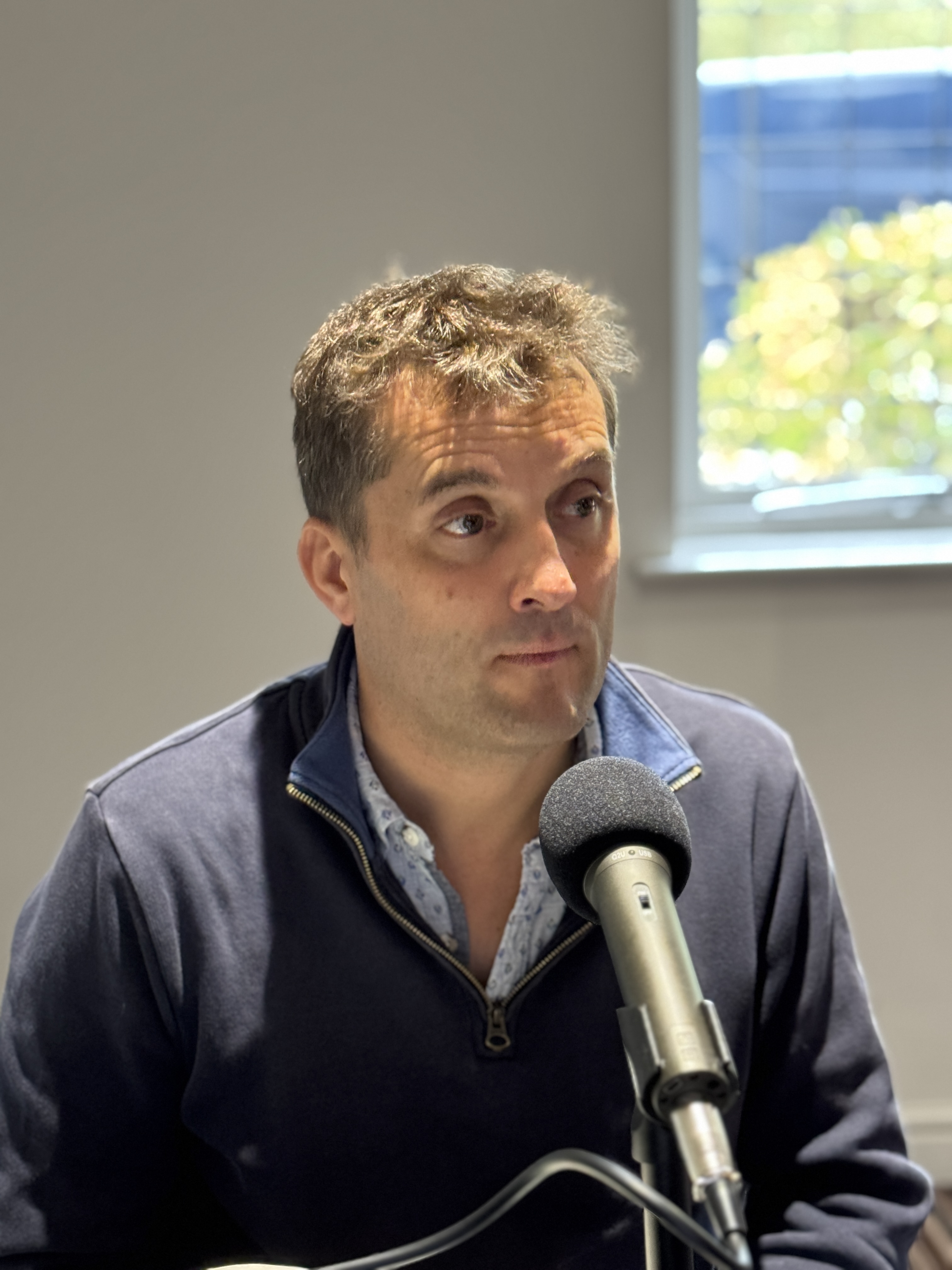 Iain Beardsell seated at a microphone while recording a podcast.