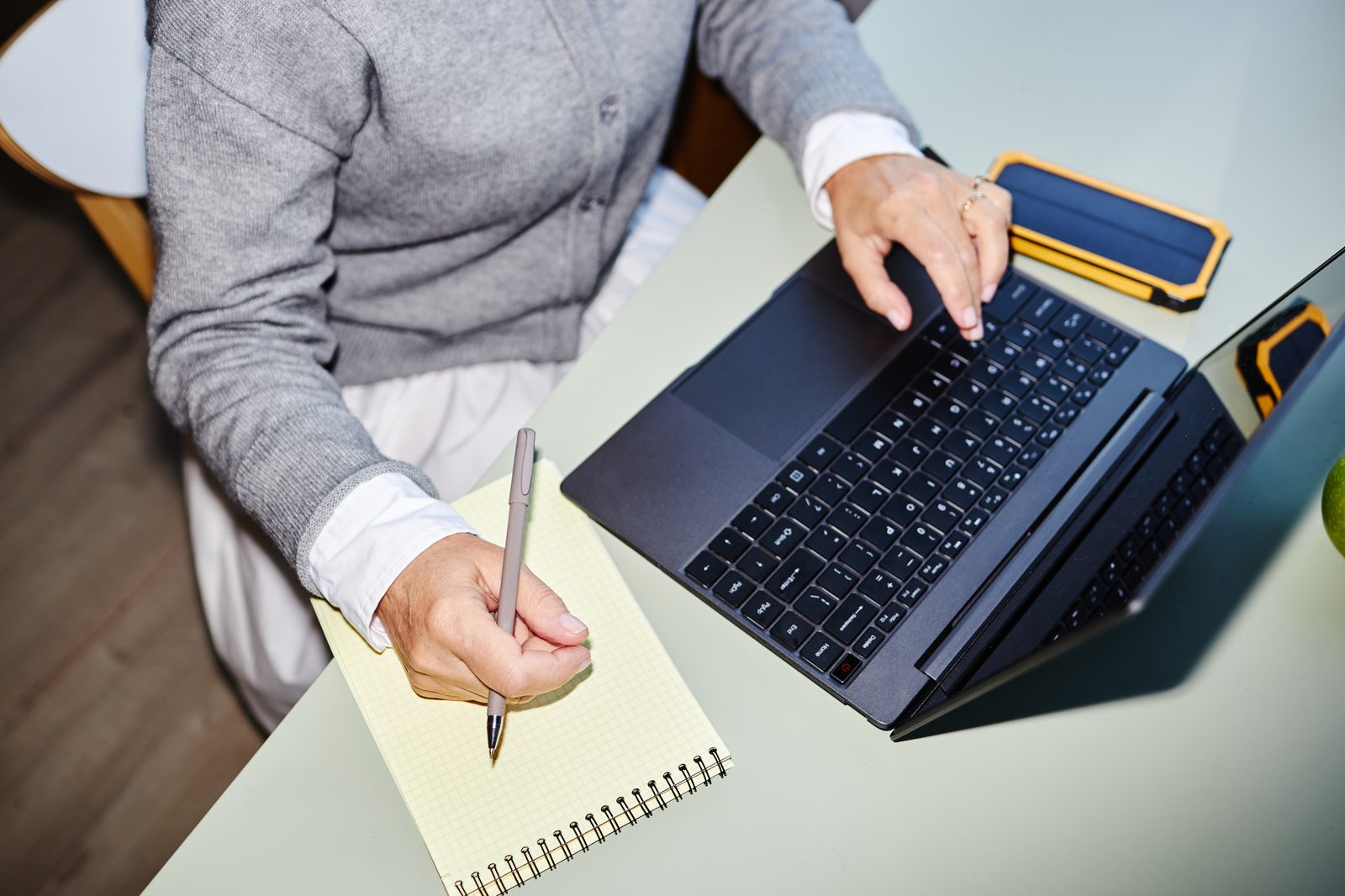 Iemand werkt aan een laptop, met een notitieblok en telefoon ernaast