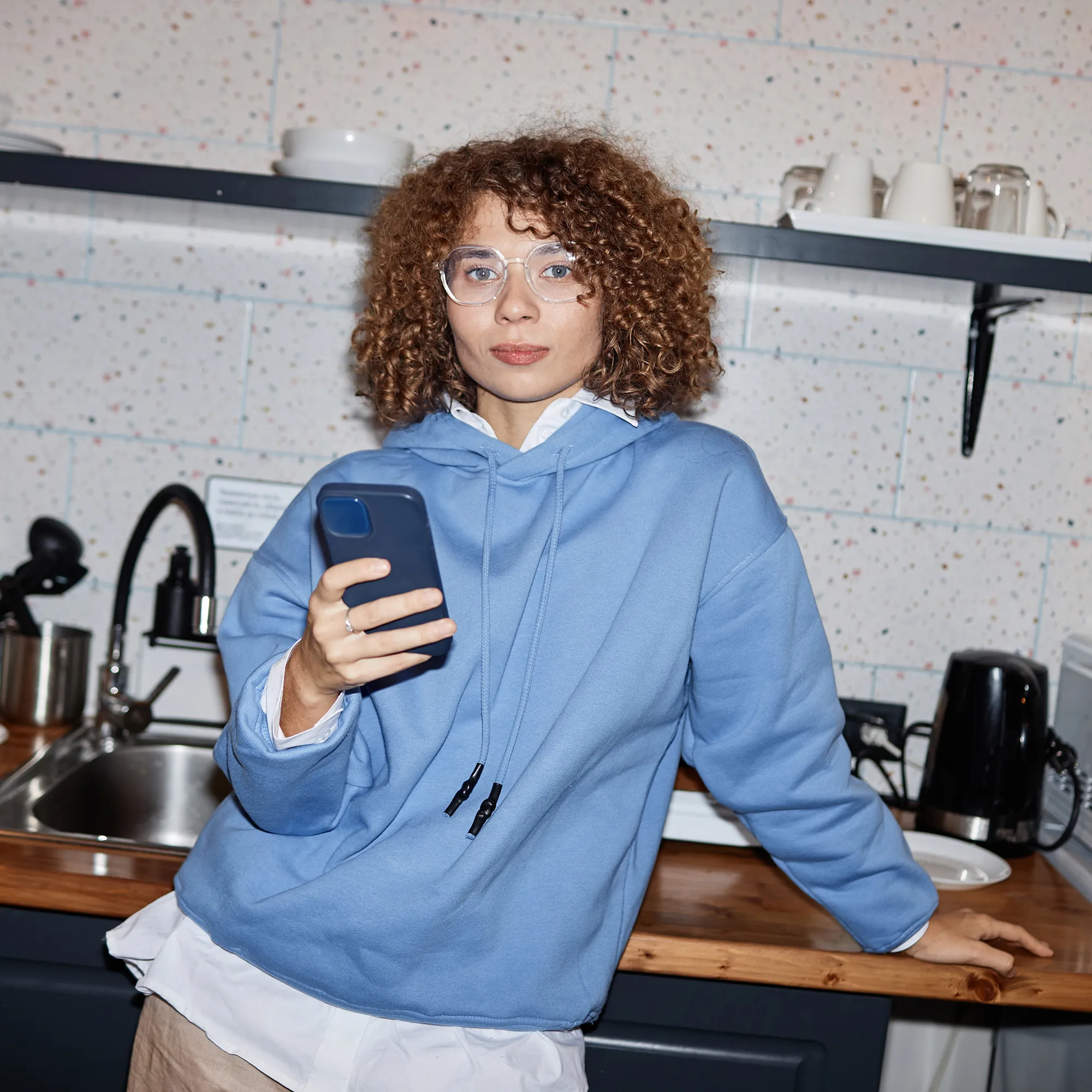 Vrouw in een blauwe hoodie kijkt op haar smartphone in een keuken