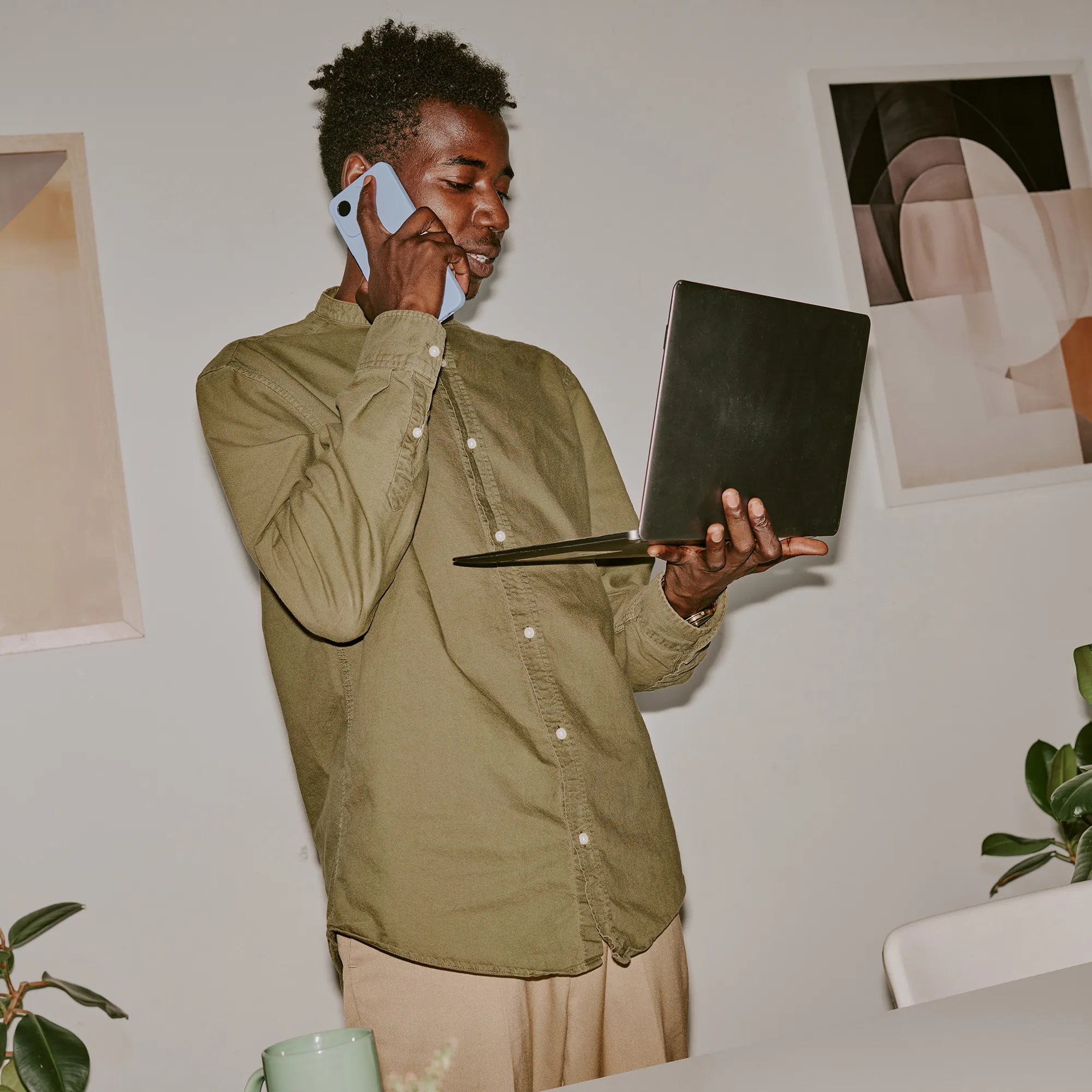 Man belt met zijn telefoon terwijl hij een laptop vasthoudt