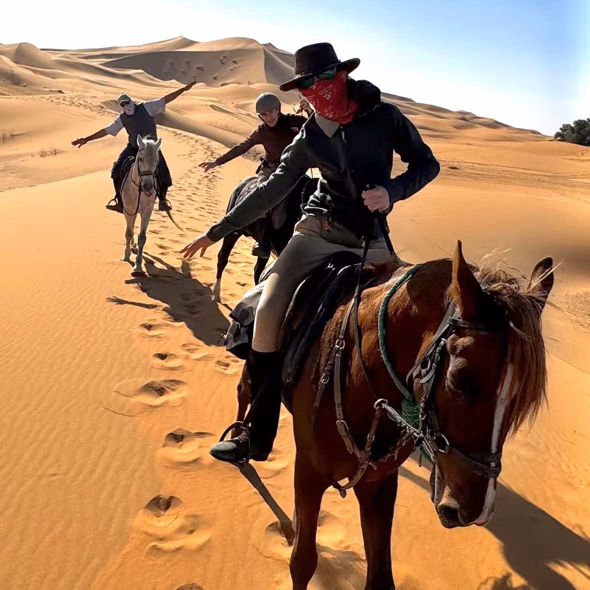 Eine Gruppe von Reitern nimmt beim Hinunterreiten einer Sanddüne lustige Posen ein.